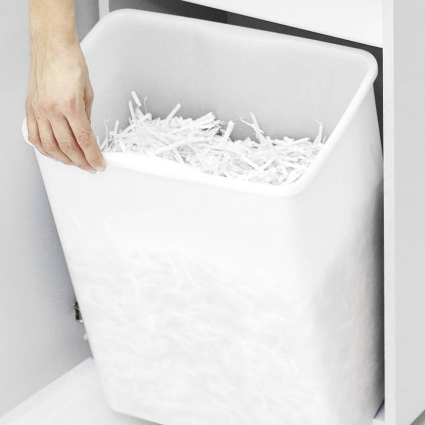 Eine Hand öffnet ein weißes Fach, in dem ein Behälter mit geschreddertem Papier sichtbar ist.