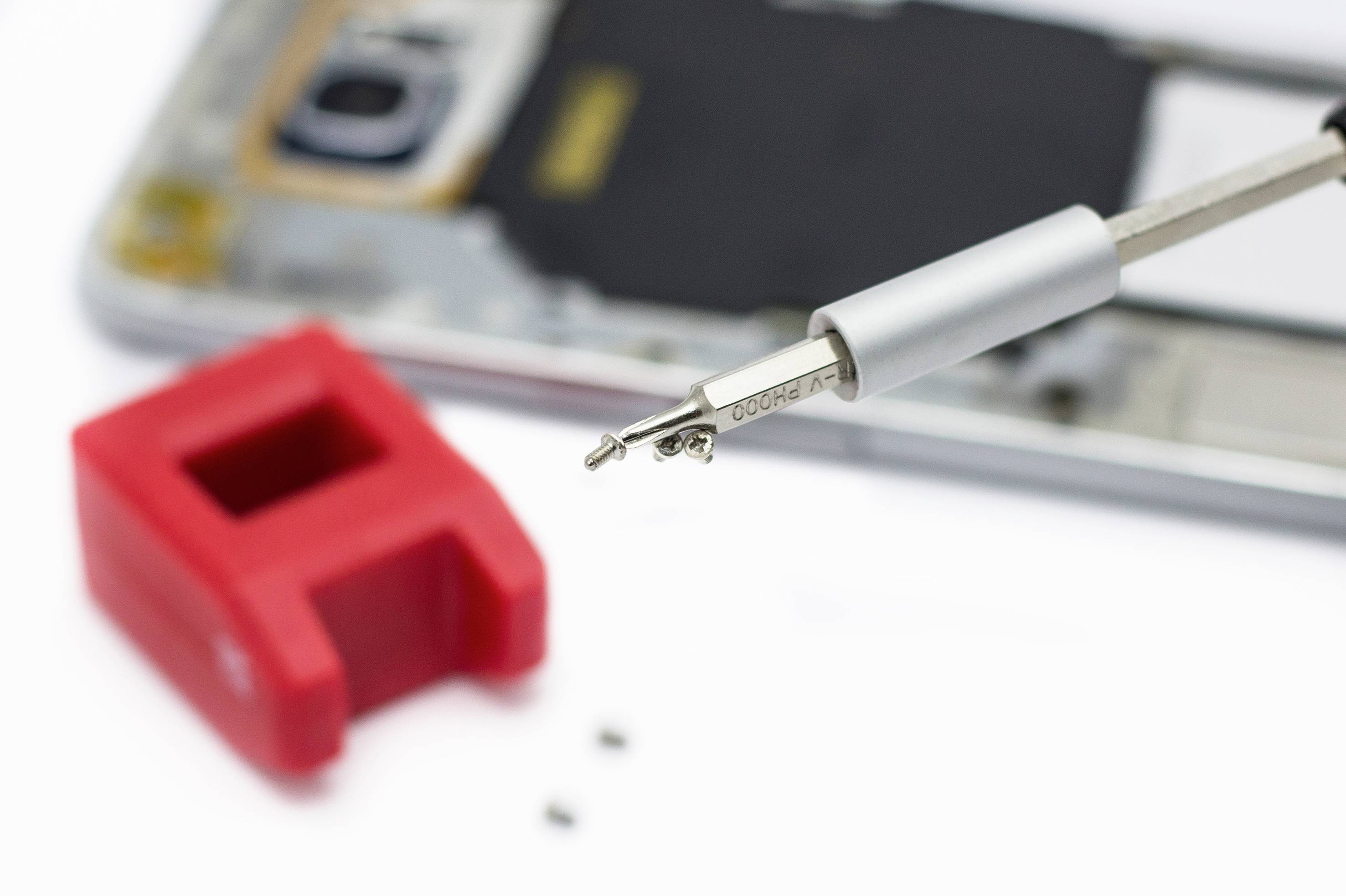 Nahaufnahme einer Metallklammer vor einem zerlegten Smartphone, zeigt präzise Reparaturwerkzeuge und Teile eines Mobilgeräts.