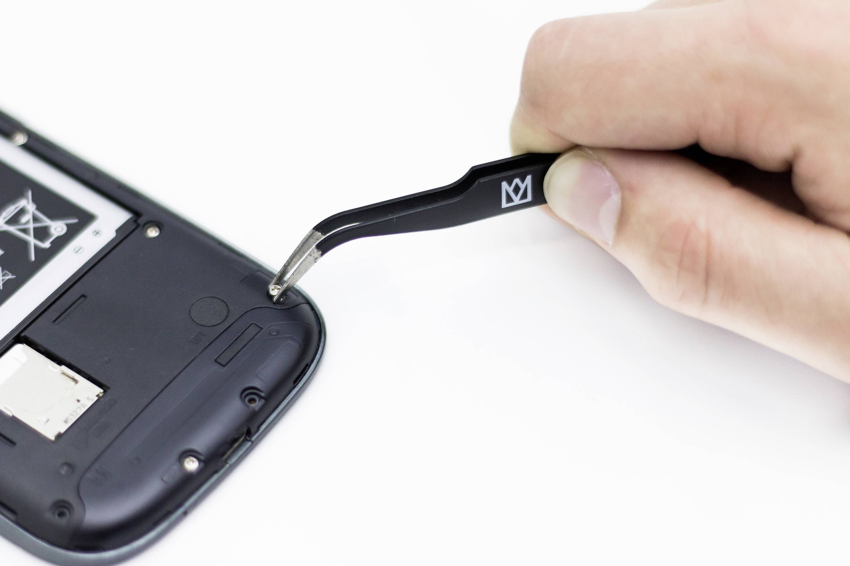 Eine Hand benutzt eine Pinzette, um an einem geöffneten Smartphone-Gehäuse einen kleinen Schraubenteil zu entfernen.