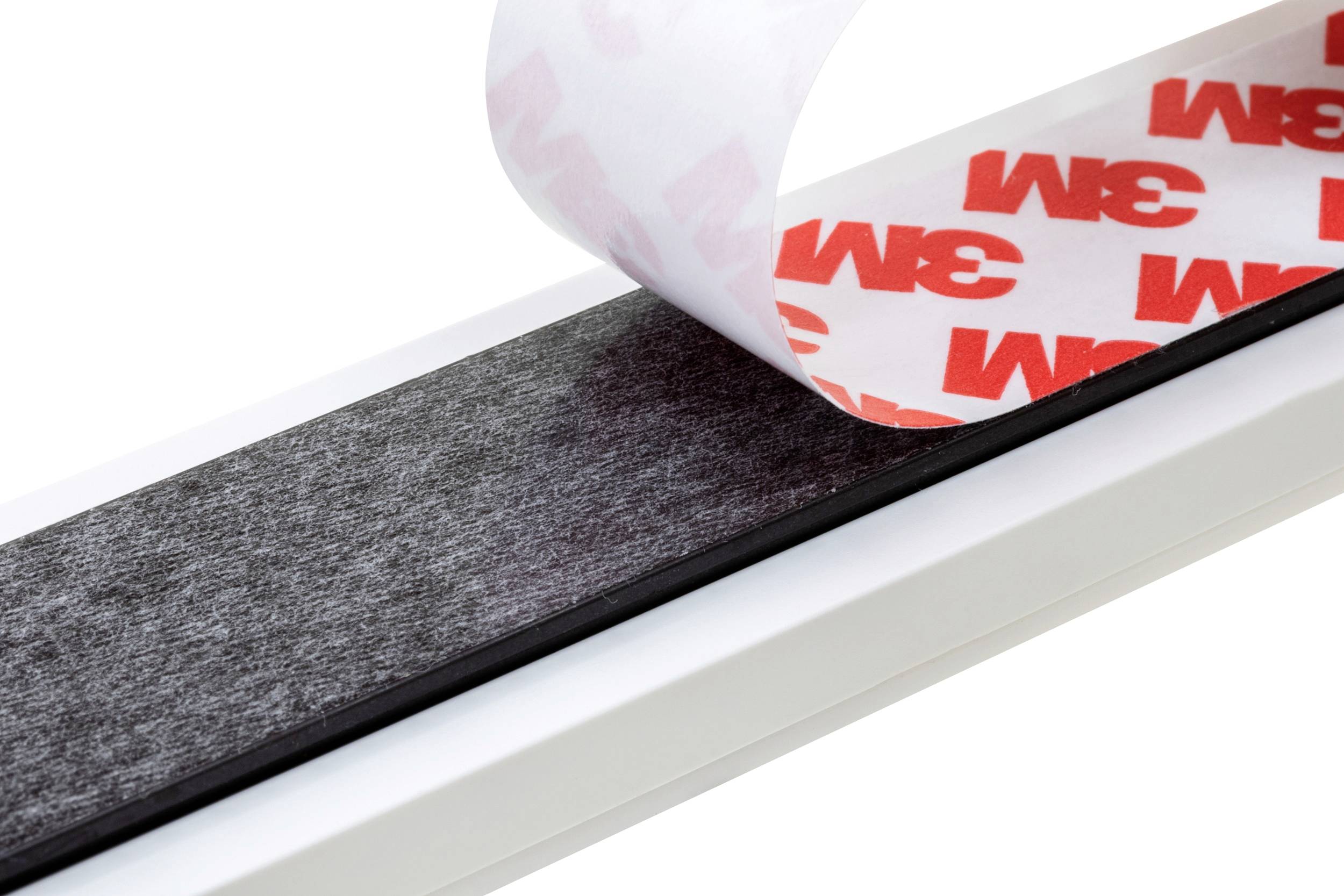 Zweiseitiges Klebeband von 3M wird von einer Oberfläche abgezogen, zeigt schwarze Verklebung und rotes Logo auf Schutzfolie.