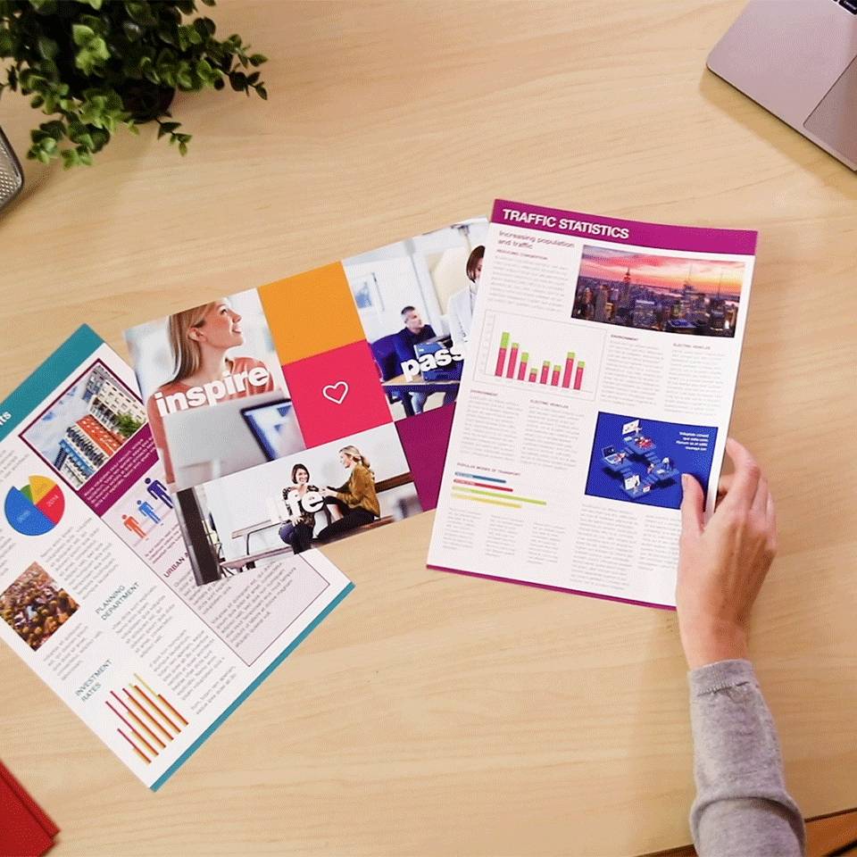 Mehrere bunte Infografiken und Broschüren liegen auf einem Tisch. Eine Hand zeigt auf ein Diagramm mit dem Titel 'Traffic Statistics'.