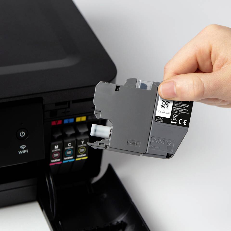 Eine Hand ersetzt eine graue Tintenpatrone in einem Drucker mit sichtbaren farbigen Tintenfächern.