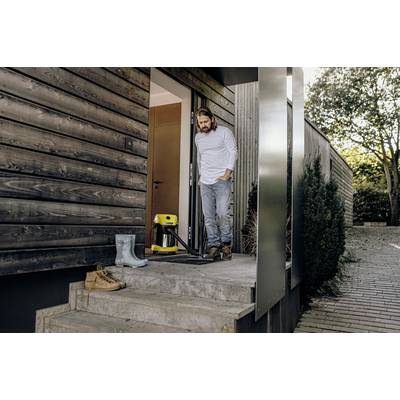 Ein Mann steht in Freizeitkleidung auf der Terrasse eines modernen Holzhauses. Neben ihm steht ein gelber Hochdruckreiniger.