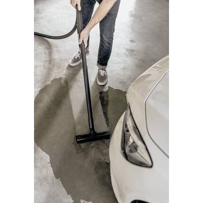 Person saugt eine Wasserpfütze mit einem Nasssauger auf, nahe einem weißen Auto in einer Garage.