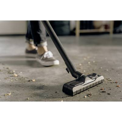 Eine Person saugt mit einem Staubsauger schmutzigen Boden. Man sieht nur die Schuhe und den Staubsauger, während Verschmutzungen entfernt werden.