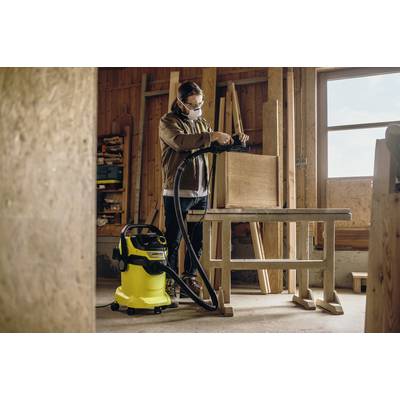 Ein Tischler arbeitet in einer Werkstatt, nutzt einen Staubsauger, um Holzspäne von einem Arbeitstisch zu entfernen.