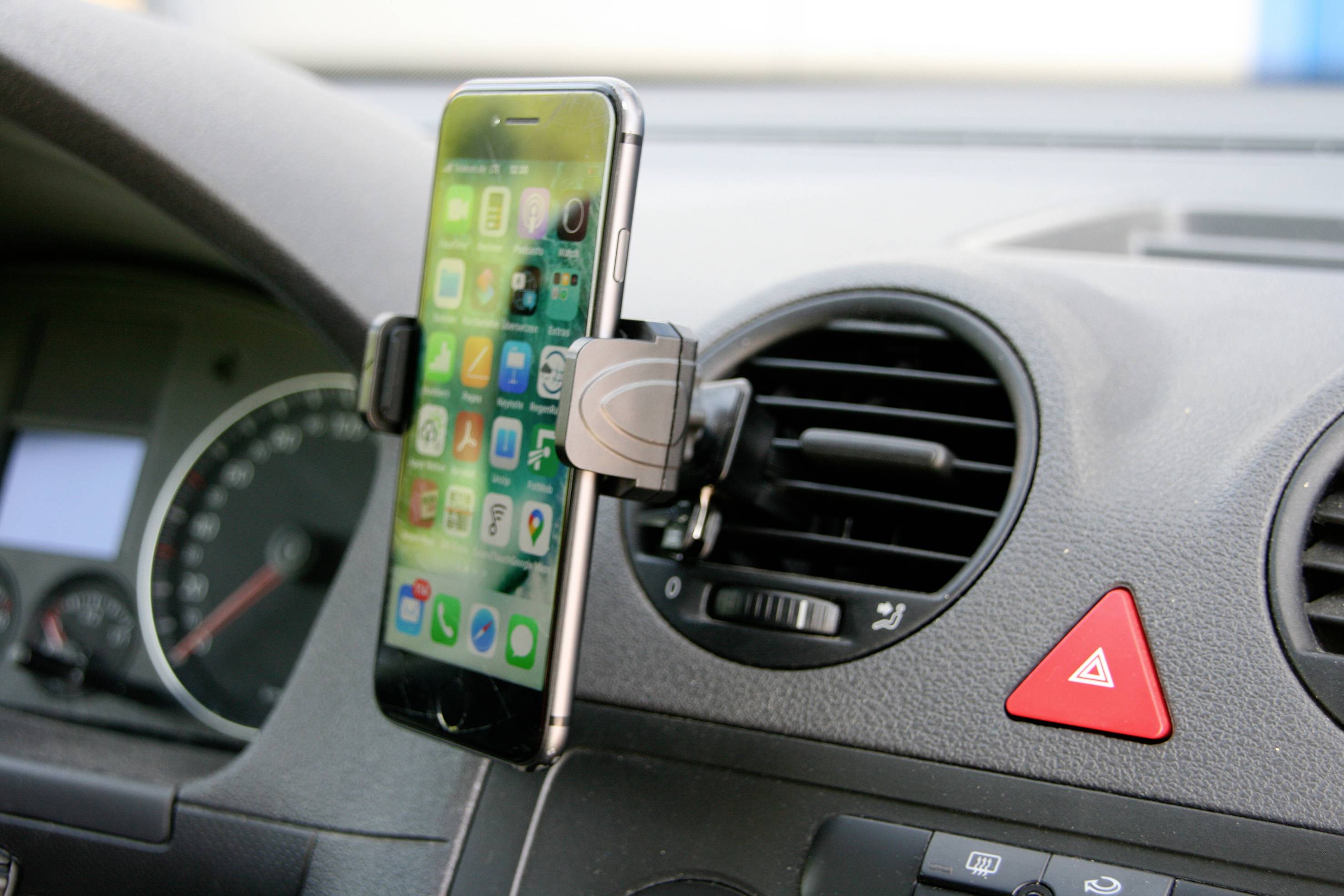 Ein Smartphone ist in einer Halterung am Lüftungsschlitz eines Autos befestigt, das Display zeigt verschiedene Apps.