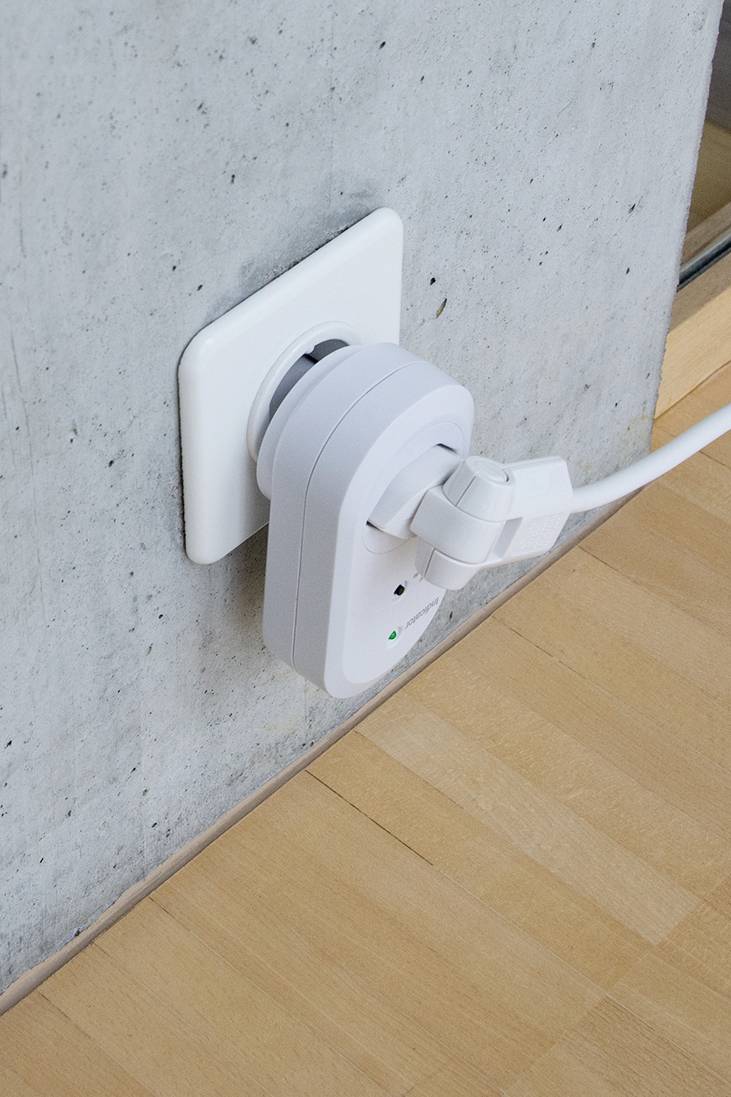 Eine weiße Steckdose an einer Betonwand mit einem eingesteckten elektrischen Gerätadapter. Ein weiteres Kabel ist dort angeschlossen.