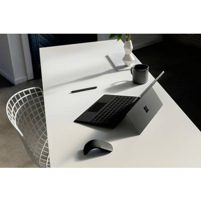 Ein moderner Arbeitsplatz mit einem Laptop, einer Maus, einem Stift, einer Tasse und einer Vase auf einem weißen Tisch neben einem Metallstuhl.