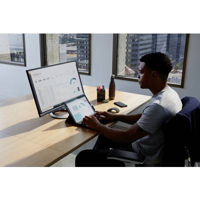 Ein Mann arbeitet in einem Büro an einem Laptop und einem Monitor, auf denen Geschäftsdatenanalysen mit Diagrammen und Tabellen angezeigt werden.