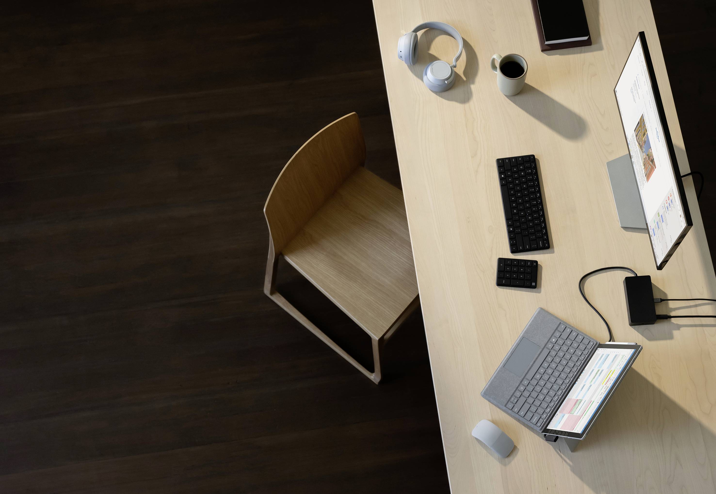 Ein Schreibtisch mit einem Laptop, zwei Monitoren, einer Tastatur, einer Maus, einem Smartphone, Kopfhörern und einer Kaffeetasse.