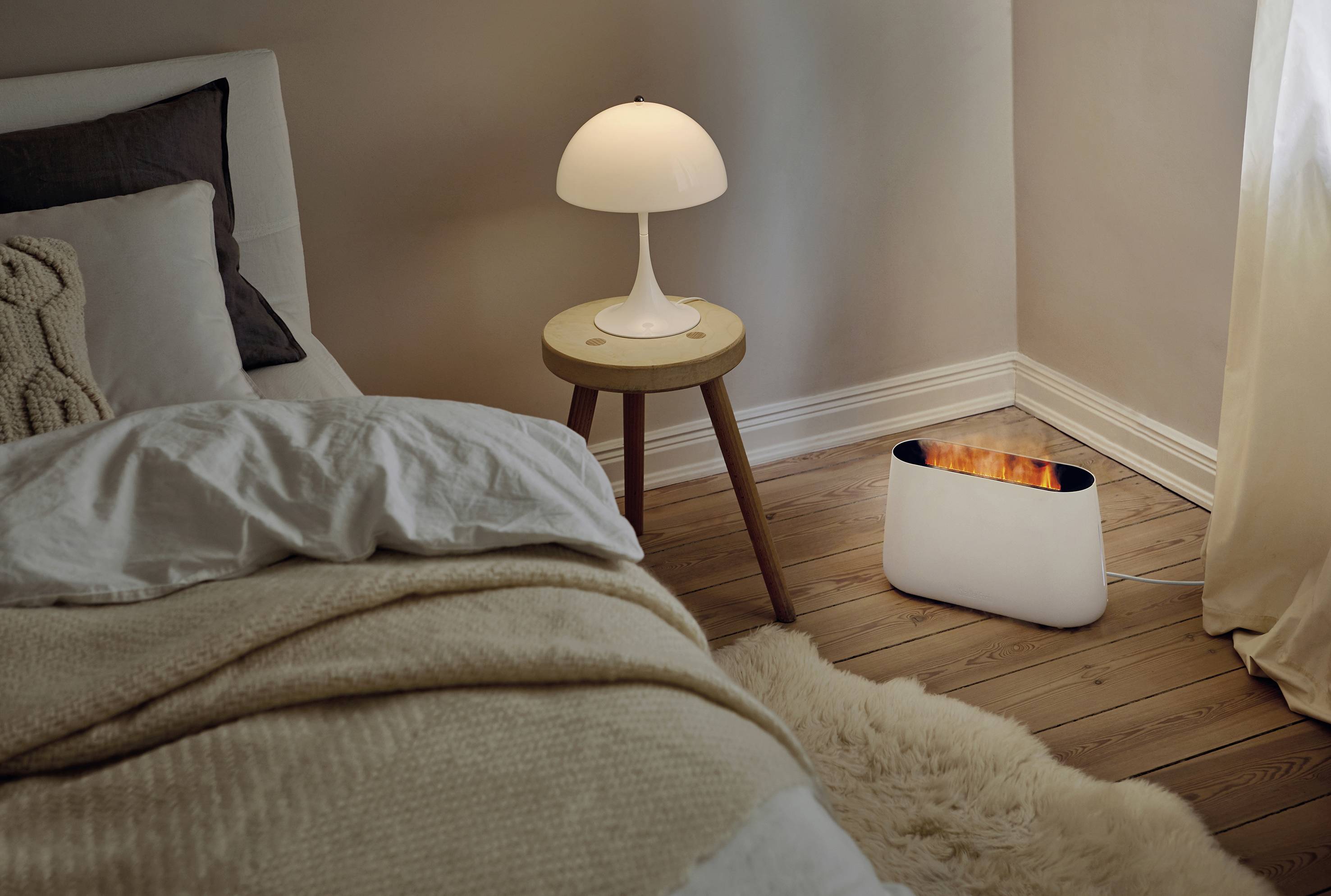 Ein gemütliches Schlafzimmer mit einem Bett, Nachttisch und Lampe. Auf dem Boden steht ein weißes Gerätegehäuse neben dem Bett.