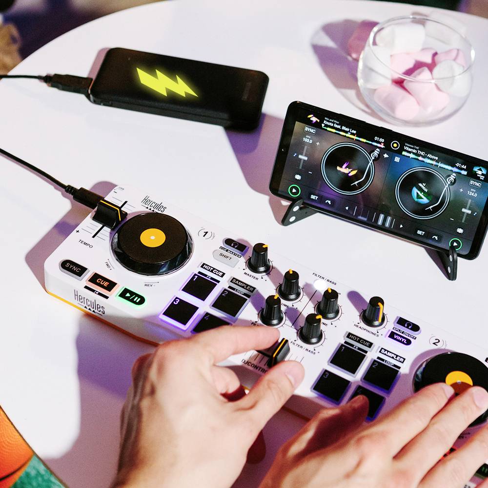 Person mixt Musik mit einem DJ-Controller, verbunden mit einem Smartphone auf einem Tisch.