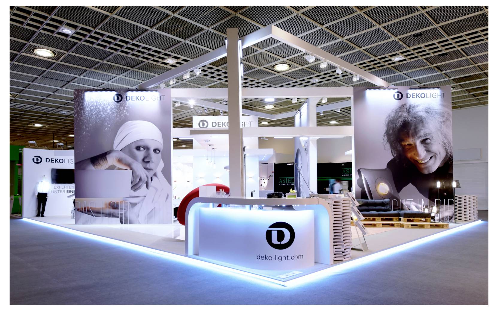 Messestand für Dekolight mit beleuchtetem Tresen, Präsentationswänden und großformatigen Porträtgrafiken unter einer beleuchteten Rahmenkonstruktion.