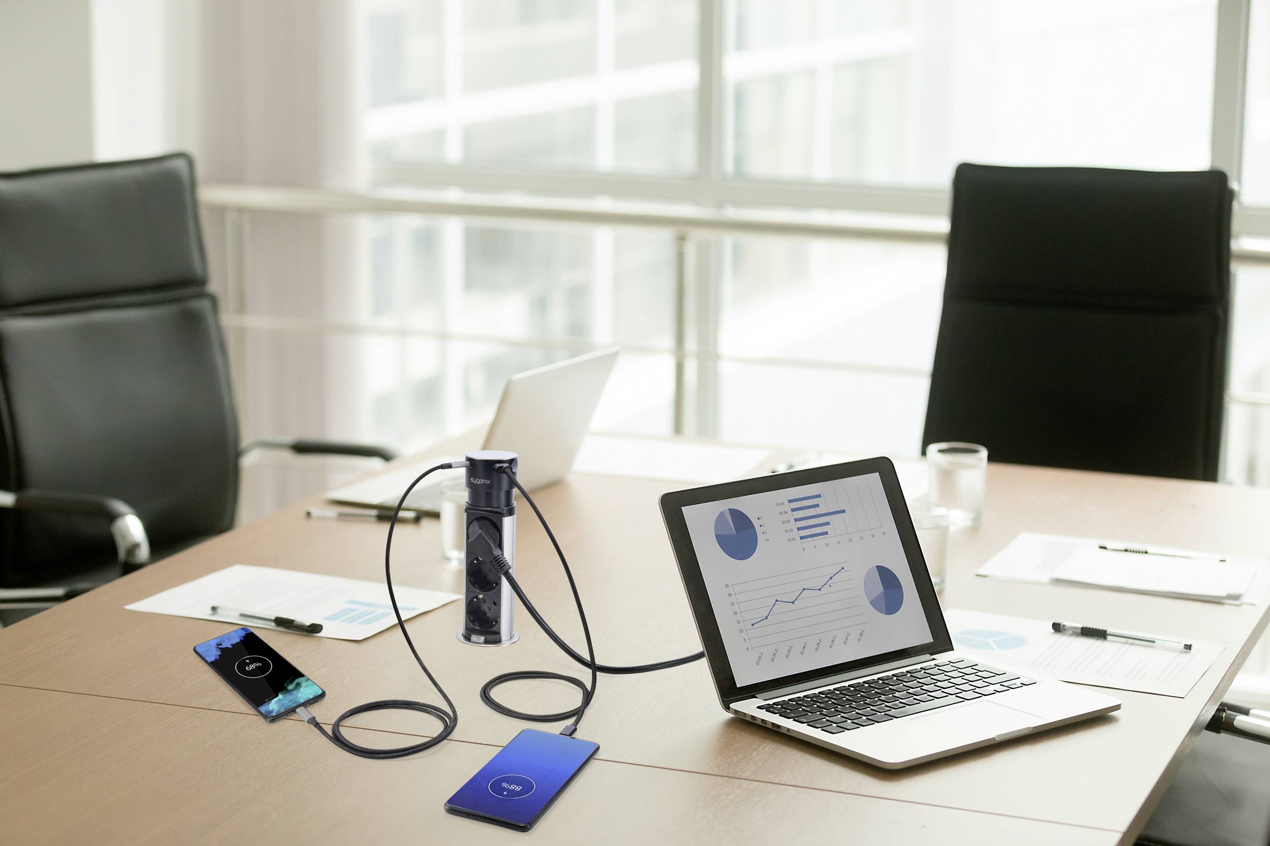 Ein Konferenzraum mit einem Laptop auf einem Tisch zeigt Finanzdiagramme auf dem Bildschirm. Zwei leere Stühle und Dokumente im Hintergrund.