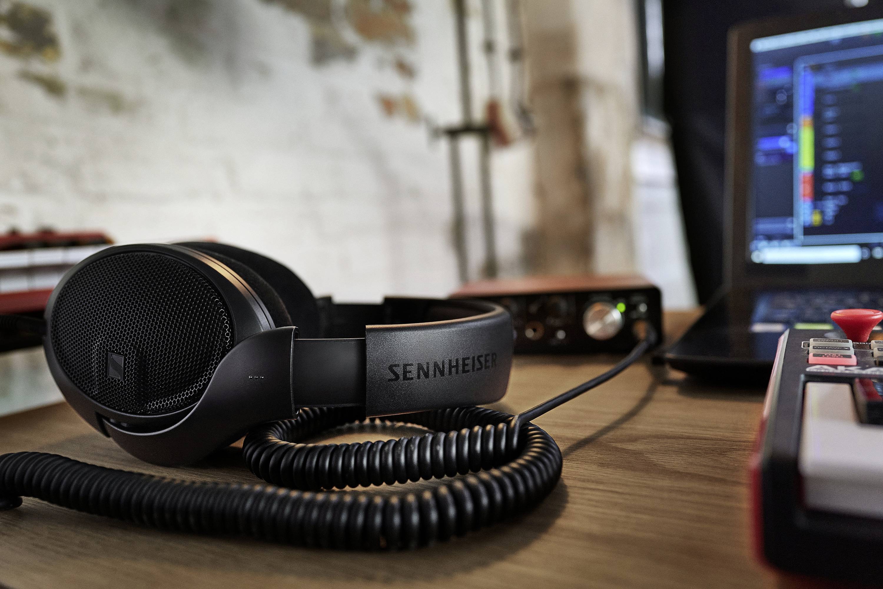 Sennheiser-Kopfhörer liegen auf einem Tisch neben einem Laptop mit geöffneter Musiksoftware und Audio-Interface, in kreativem Raum.