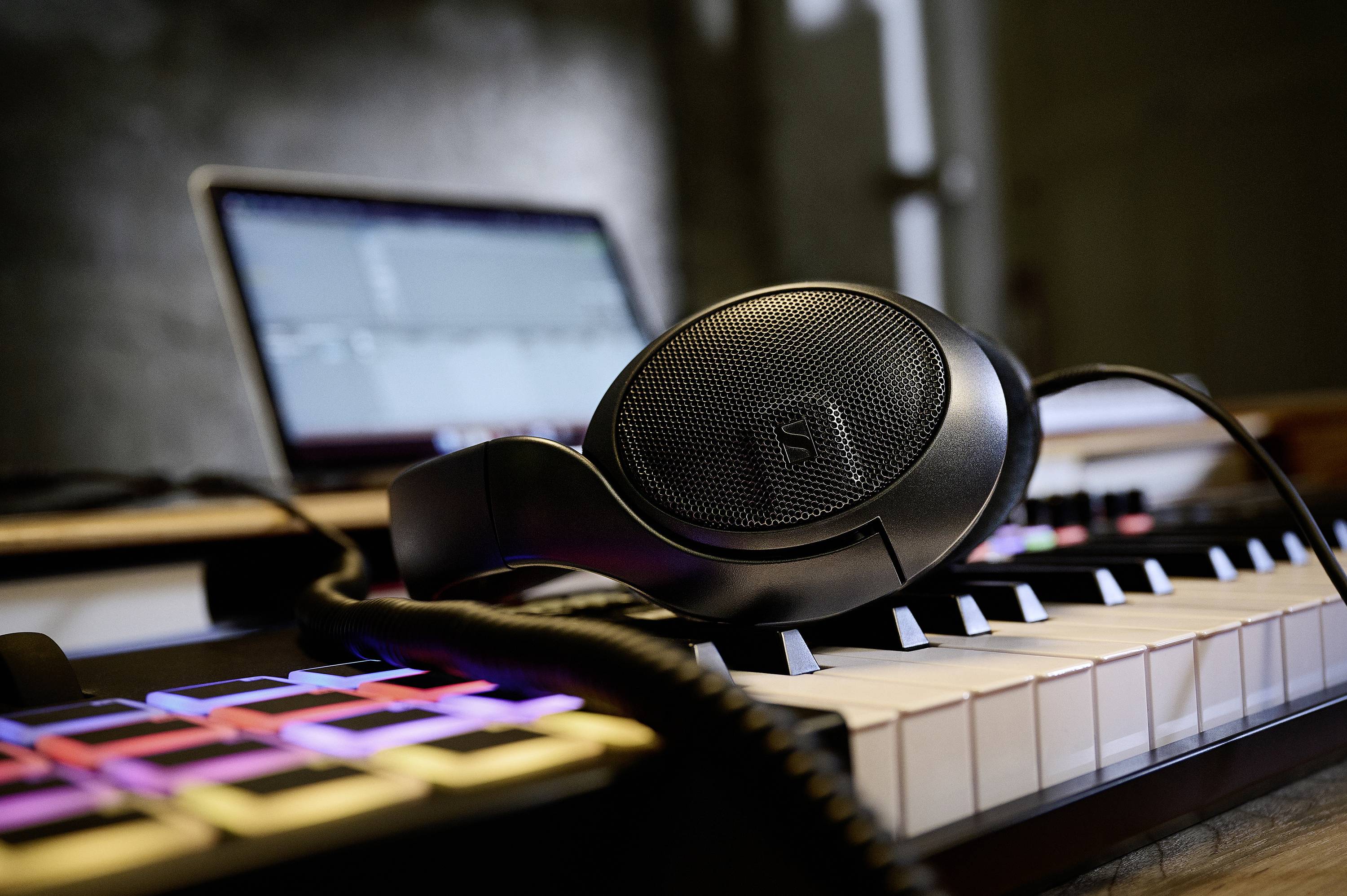 Kopfhörer liegen auf einem Keyboard, im Hintergrund ein verschwommener Laptop. Musikalisches Arbeitsumfeld.