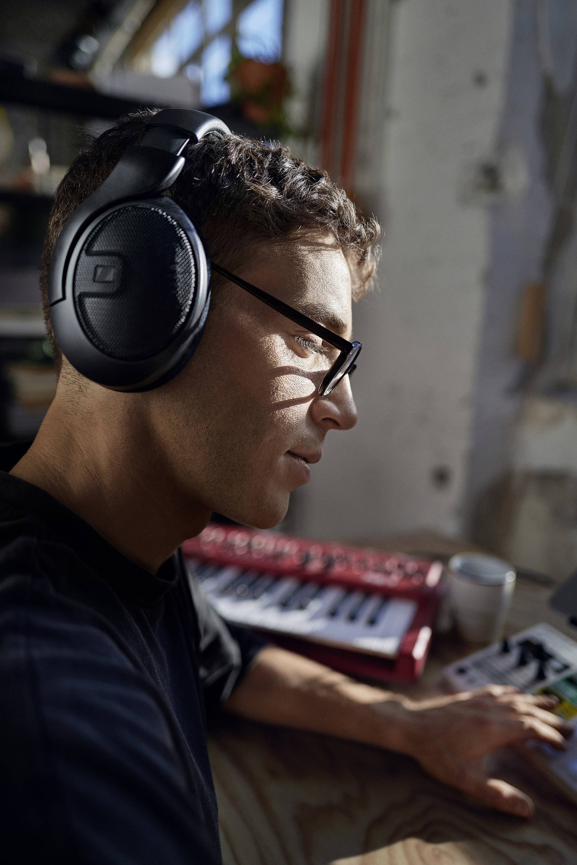 Eine Person trägt Kopfhörer und arbeitet an einem Musik-Mischpult in einem sonnendurchfluteten Raum, im Hintergrund eine Pflanze.