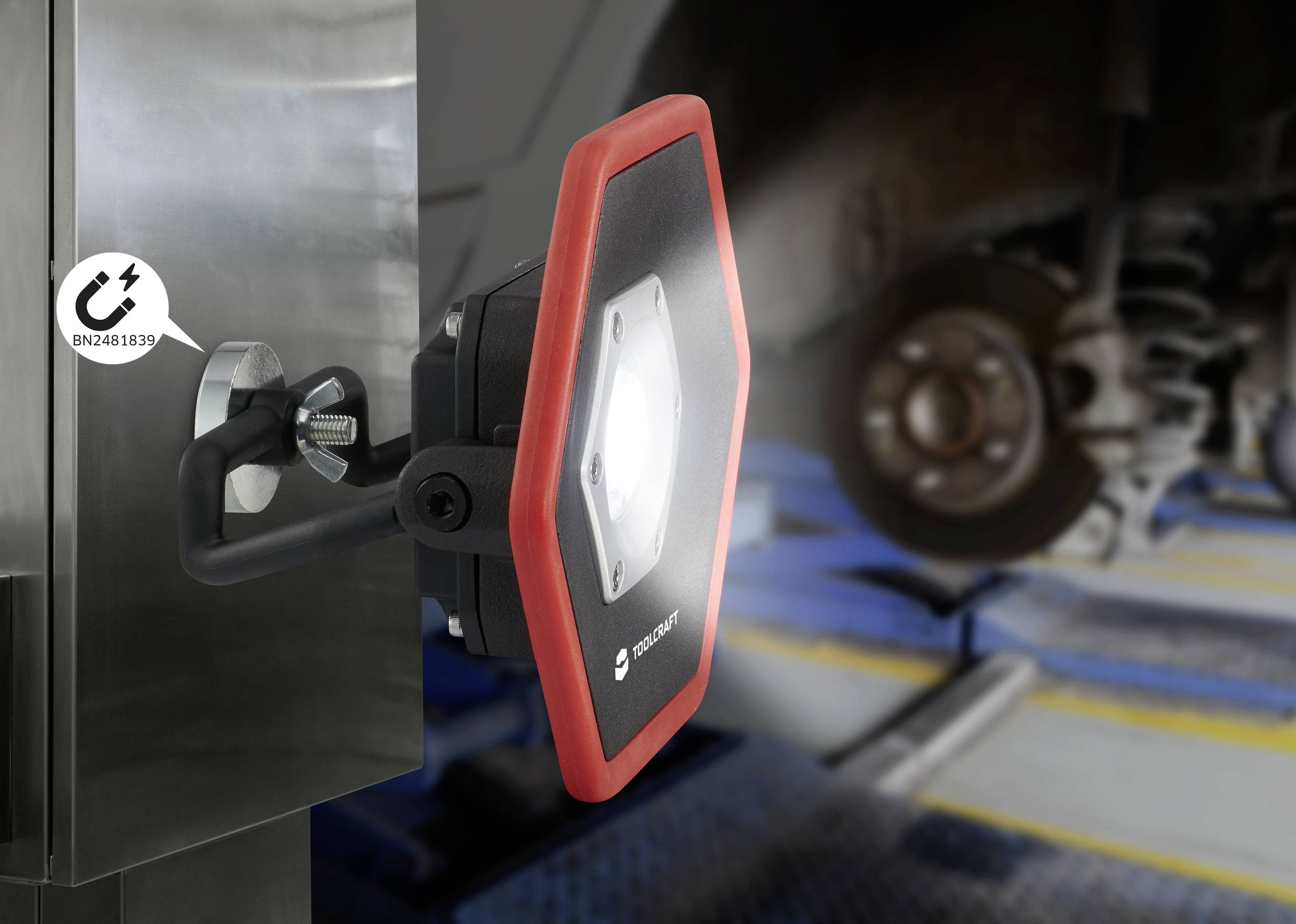 Ein Werkstatt-Scheinwerfer leuchtet auf ein Fahrgestell eines Fahrzeugs in einer Autowerkstatt. Der Scheinwerfer ist an einem Metallträger befestigt.