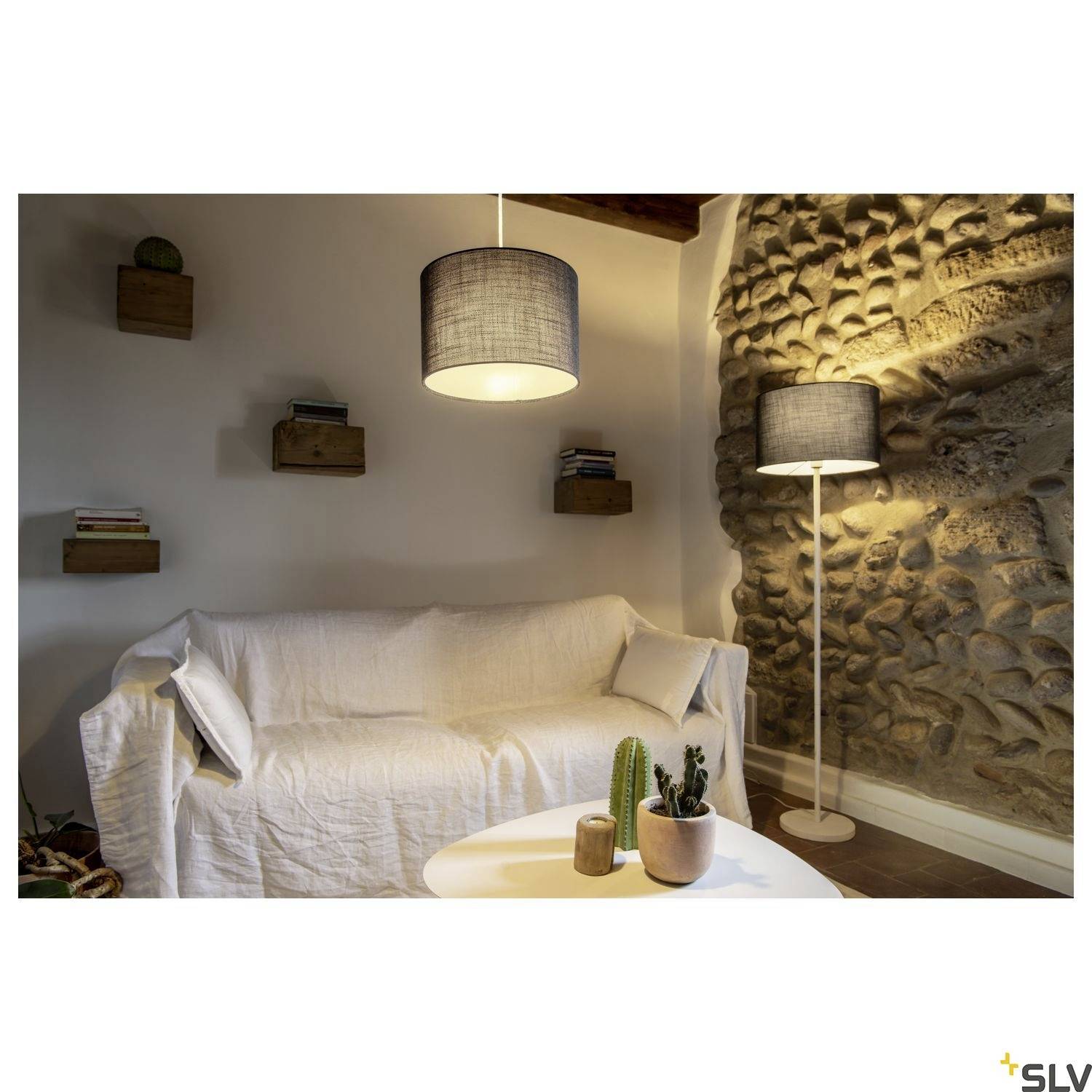 Wohnzimmer mit weißem Sofa, hängenden Holzregalen mit Büchern, zwei Lampen und kleinem Tisch mit Pflanzen in Töpfen.