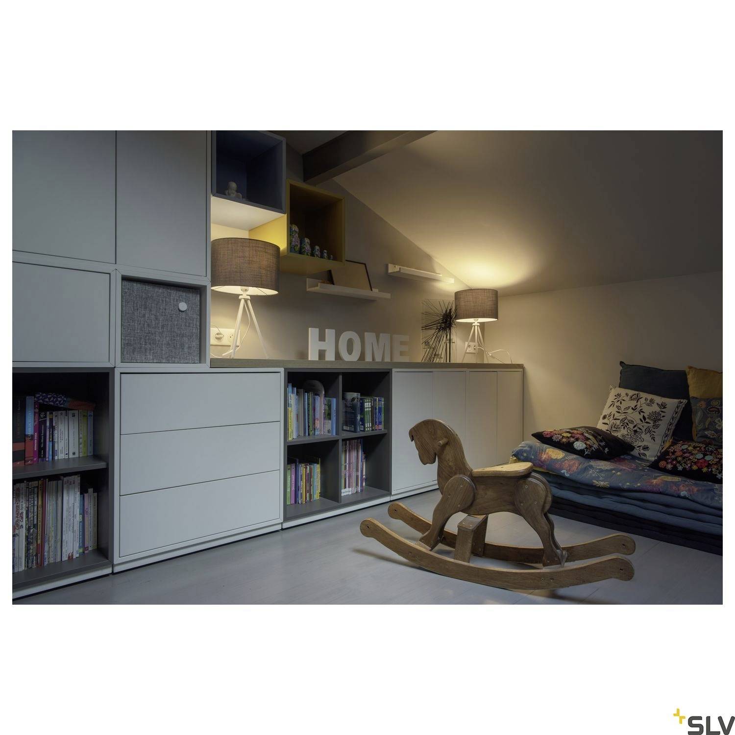 Ein Kinderzimmer mit Schrankwand, Bücherregalen und einem Schaukelpferd aus Holz. Im Hintergrund steht ein Sofa mit Kissen.