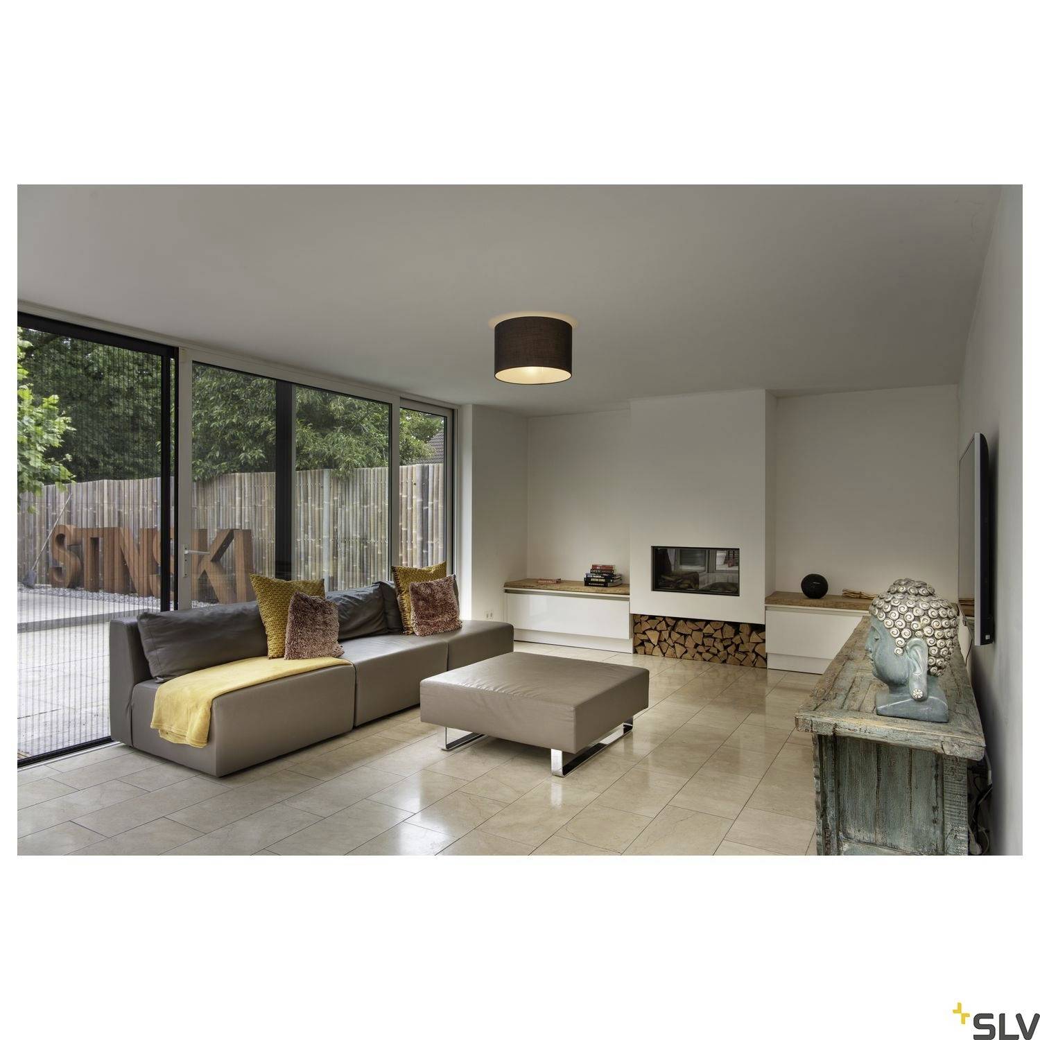 Modern eingerichtetes Wohnzimmer mit großen Fenstern, grauem Sofa, Kamin und Tisch. Außenbereich und Garten sind sichtbar.