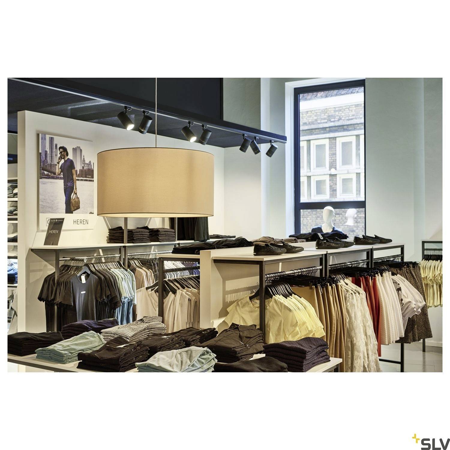 Ein Geschäft mit Regalen voll Kleidung, darunter gefaltete Shirts und gesteppte Hosen. Eine Lampe hängt über dem Verkaufsbereich.