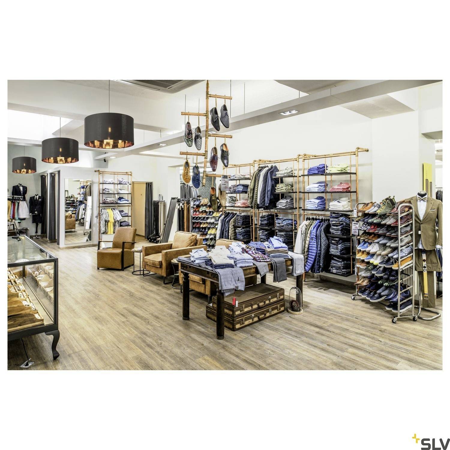 Ein Bekleidungsgeschäft mit Regalen voller gefalteter Jeans, Hemden und Schuhen. Zwei Sessel stehen in der Mitte des Raums.