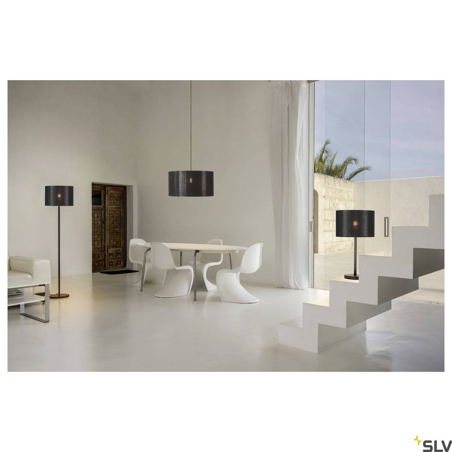 Ein modernes Wohnzimmer mit weißem Tisch und Stühlen, zwei schwarzen Stehlampen, Glastüren und einer weißen Treppe im Hintergrund.