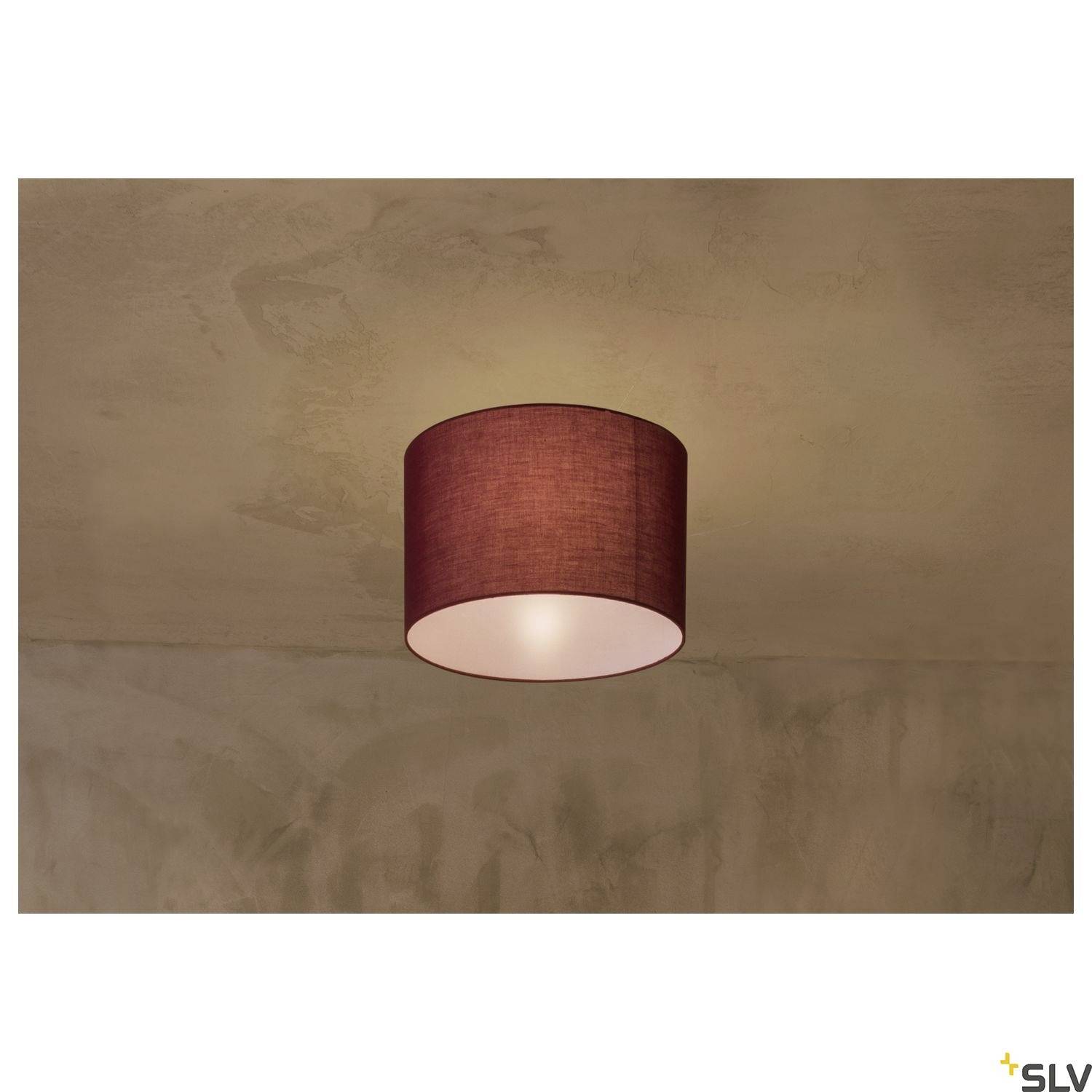 Eine schlichte Deckenlampe mit einem runden, roten Stoffschirm leuchtet weich gegen eine beige Decke und Wand.
