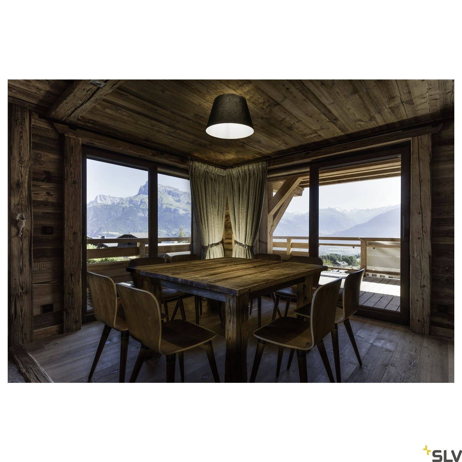 Ein rustikales, gemütliches Zimmer mit Holzwänden, Tisch und Stühlen; große Fenster bieten Bergblick.