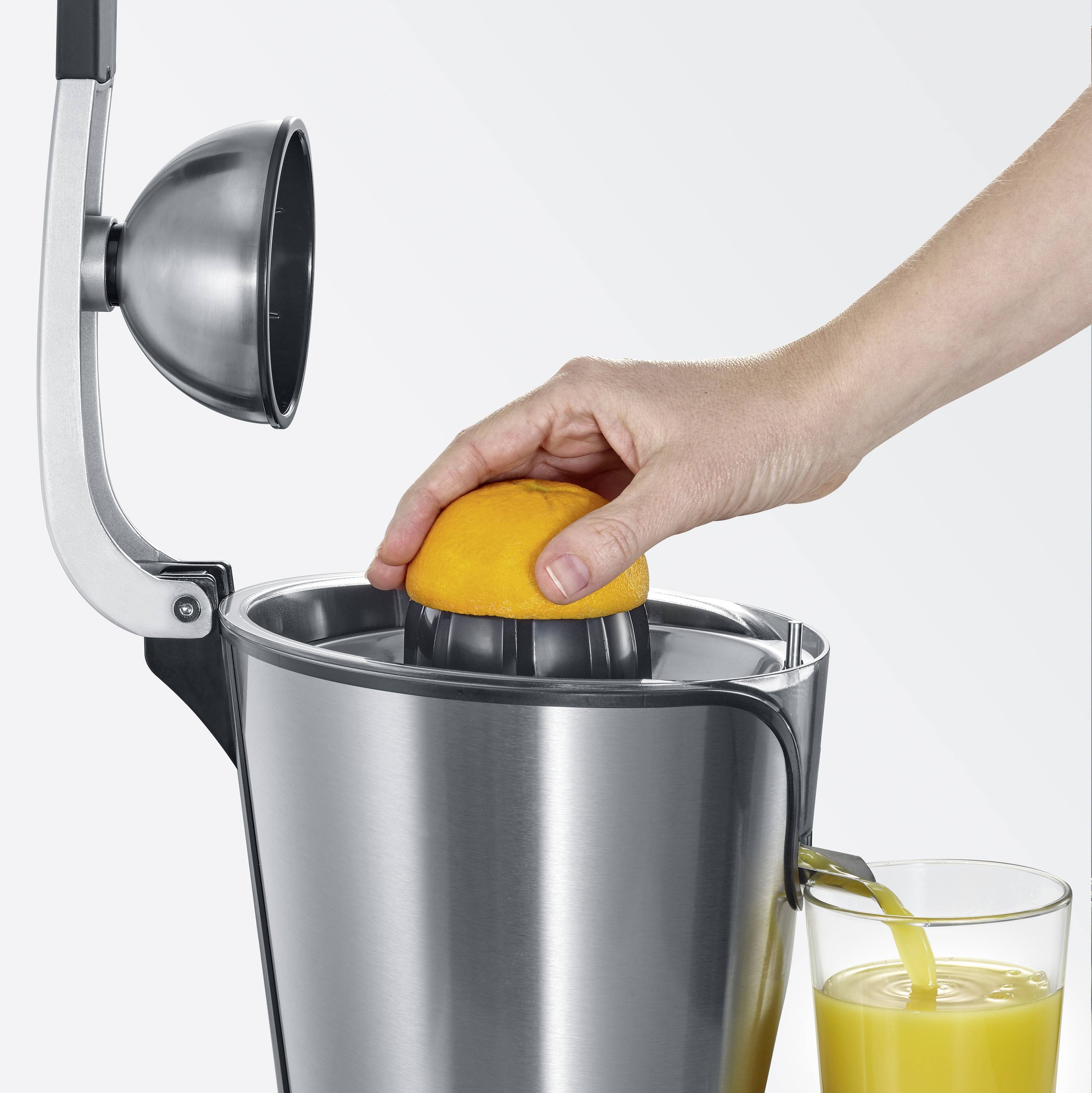 Eine Hand presst eine halbe Orange auf einer manuellen Saftpresse, während frisch gepresster Orangensaft in ein Glas fließt.