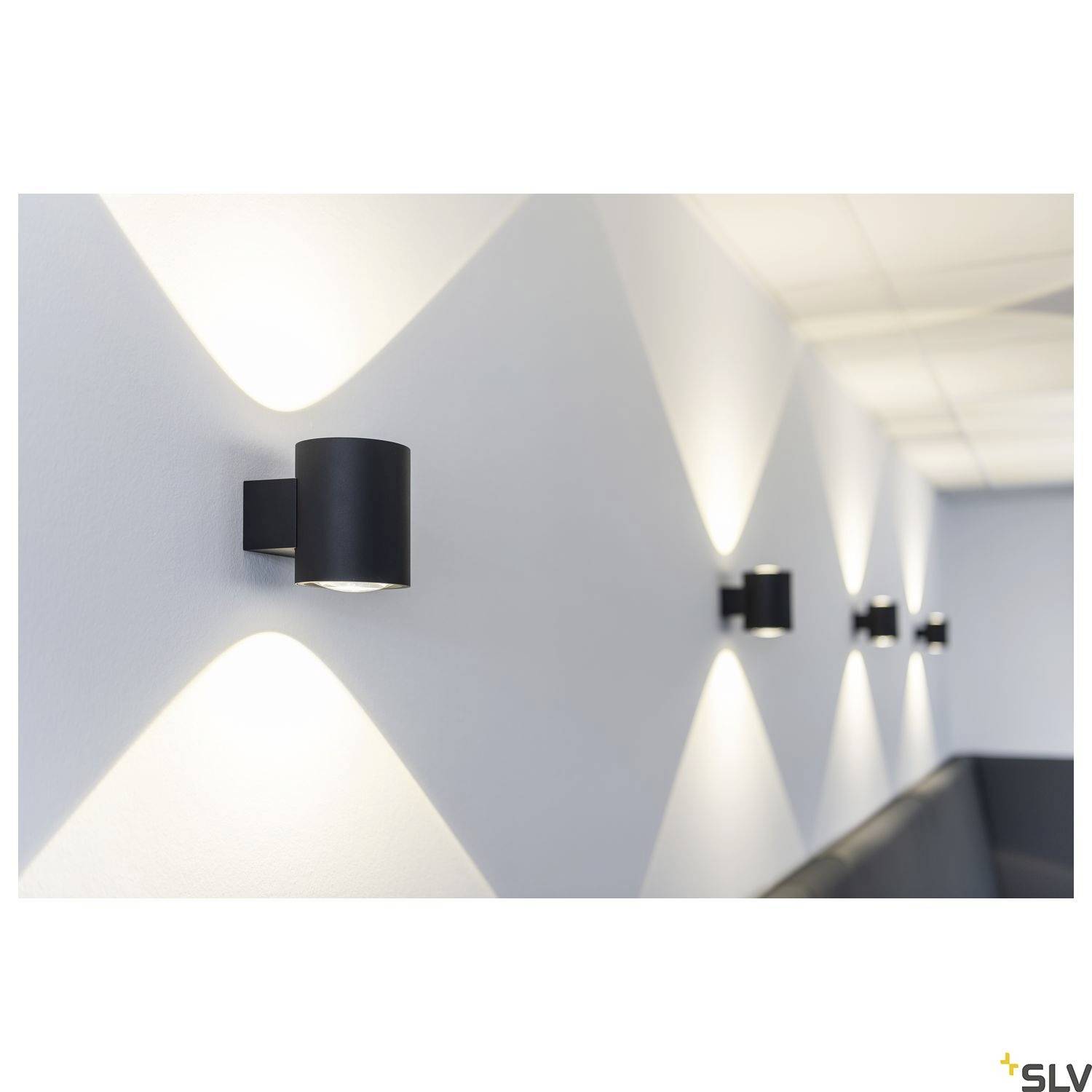 Wandleuchten erzeugen ein geometrisches Lichtmuster an einer grau gestrichenen Wand. Die Beleuchtung schafft eine moderne Atmosphäre.