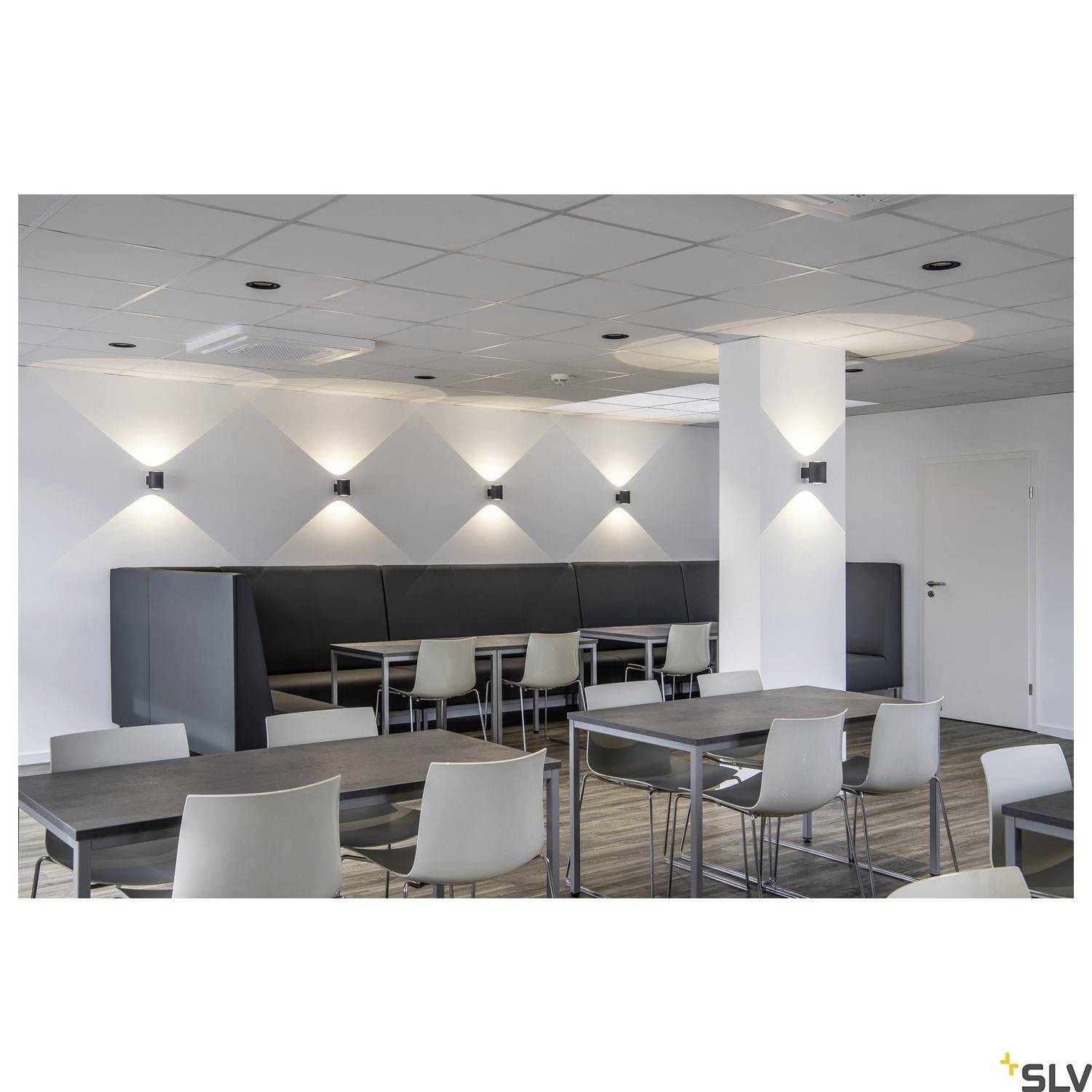 Ein moderner, gut beleuchteter Besprechungsraum mit weißen Stühlen und dunklen Tischen. An der Wand sind geometrische Lichteffekte.