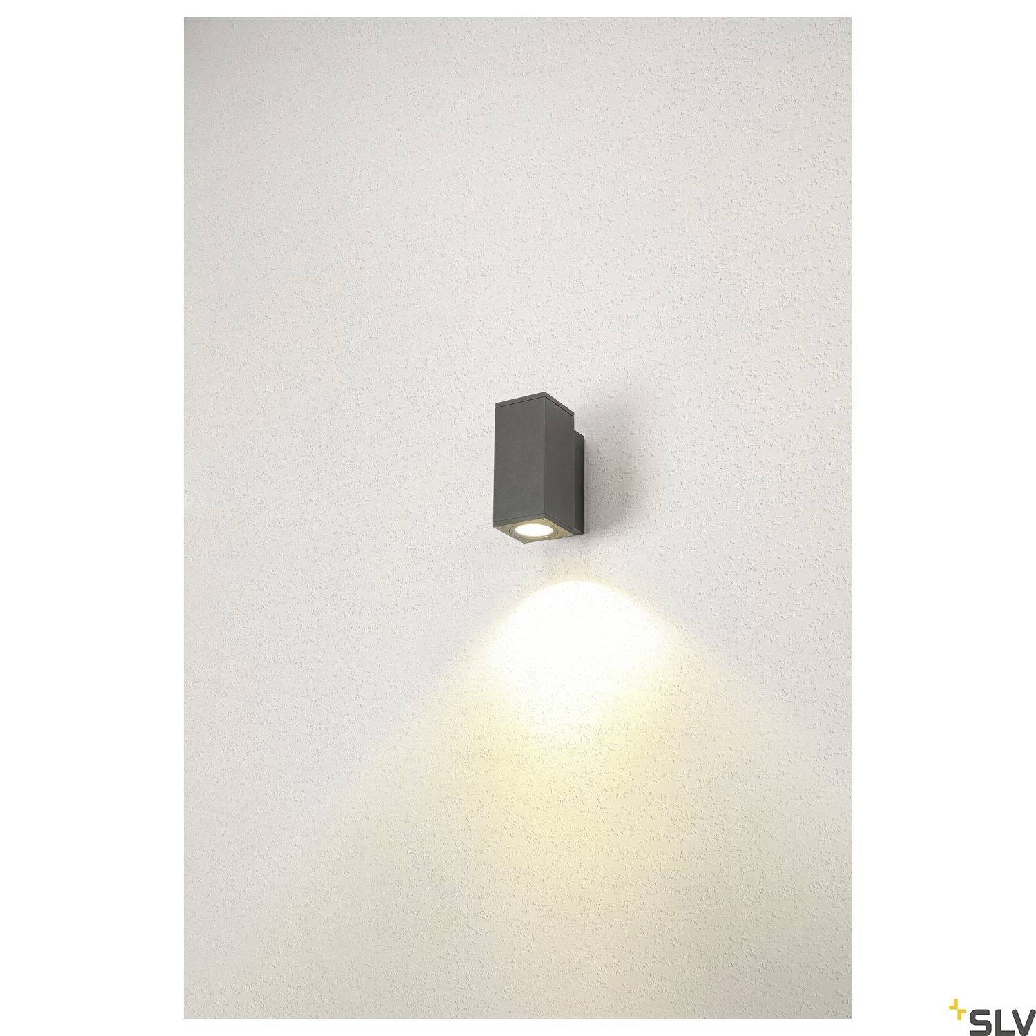 Wandlampe mit rechteckigem, schwarzen Gehäuse wirft Lichtstrahl nach unten auf weiße Wand. Schlichte, moderne Beleuchtung.