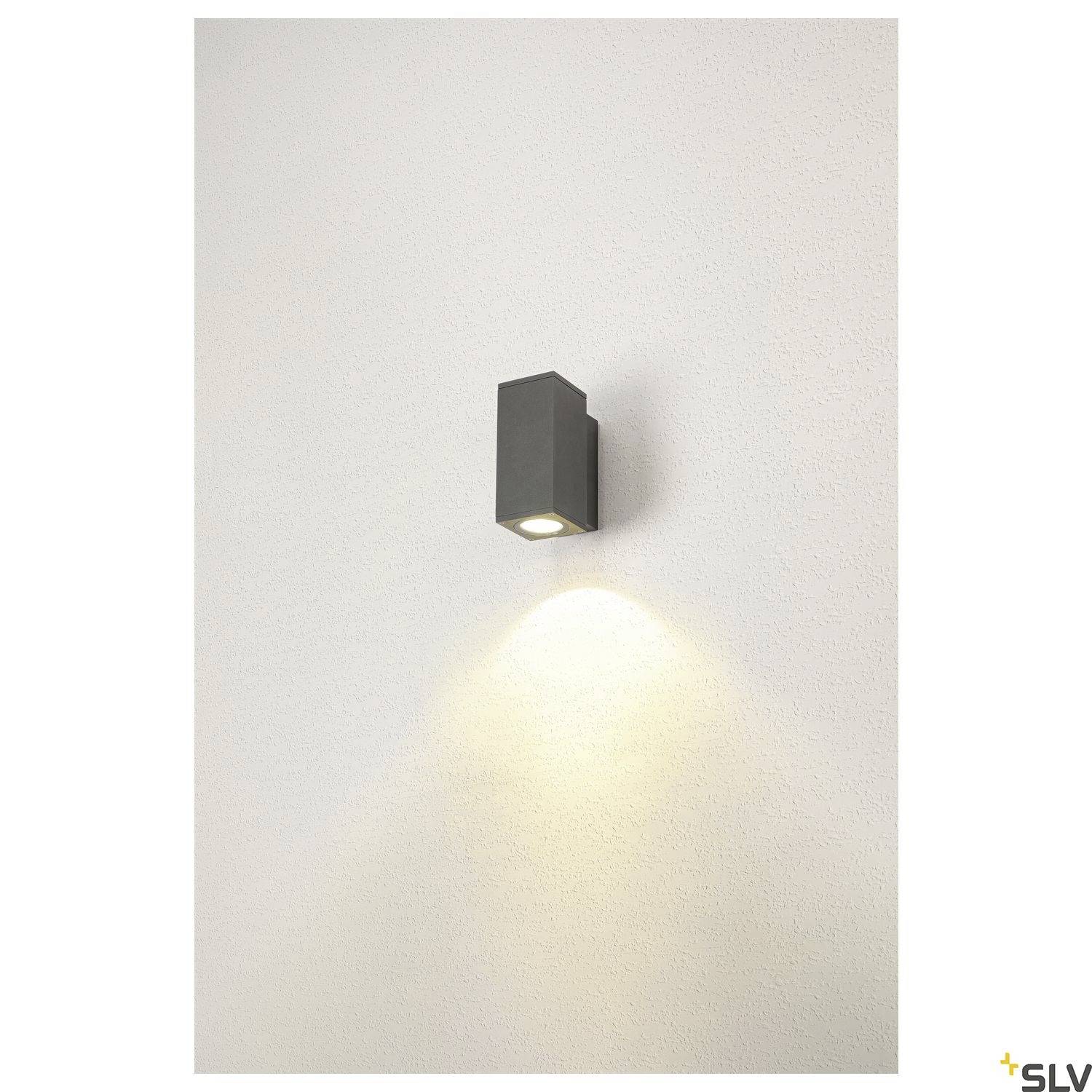 Eine rechteckige Wandleuchte ist an einer hellen Wand montiert und strahlt nach unten gerichtetes Licht aus, das auf die Wand fällt.