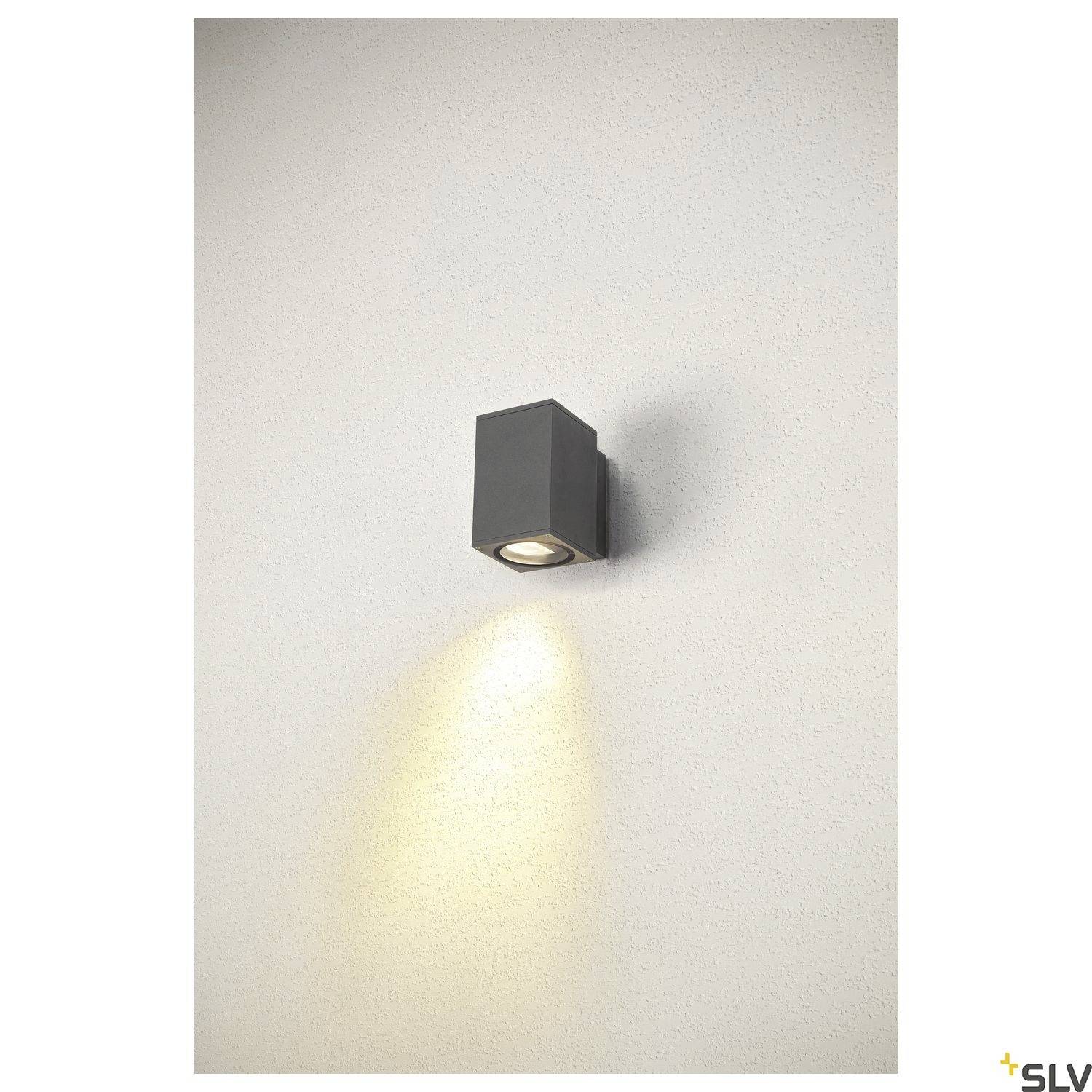 Eine schwarze Wandleuchte strahlt nach unten auf eine helle Wand. Das Licht erzeugt einen sanften Glanz direkt unter der Leuchte.