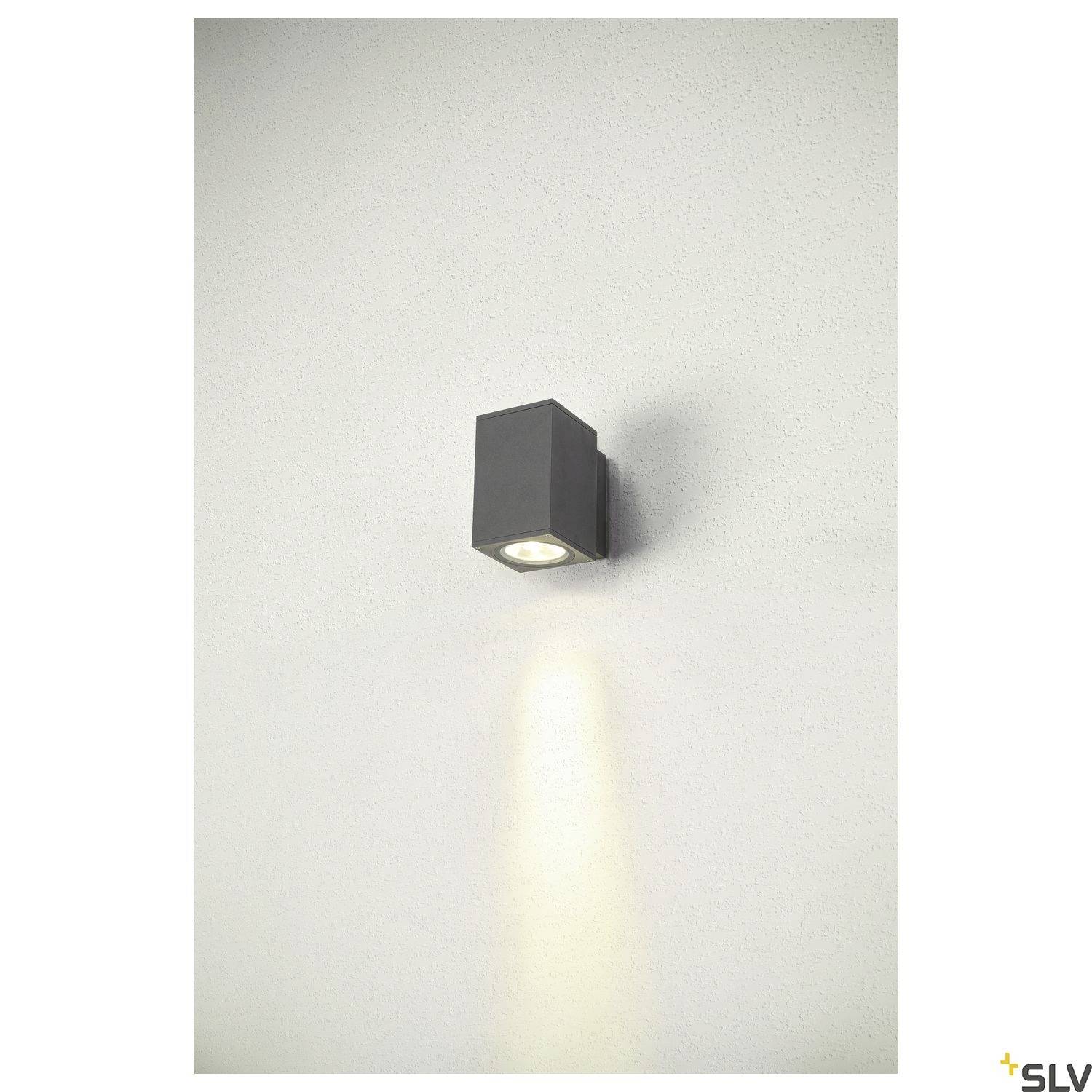 Wandleuchte mit rechteckigem Gehäuse, an einer weißen Wand montiert, strahlt Licht nach unten und beleuchtet die Wand dezent.
