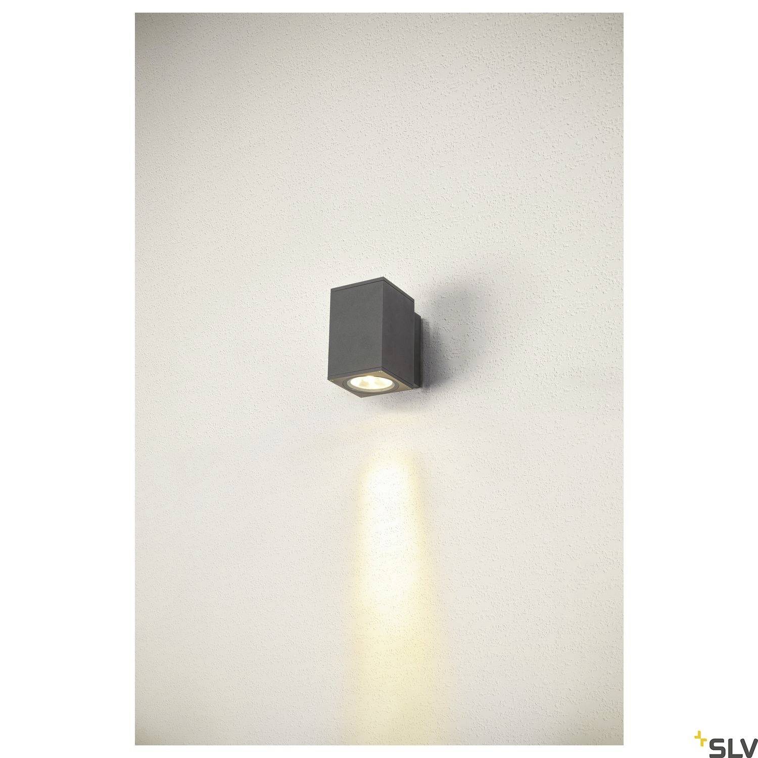 Eine schwarze, quadratische Außenleuchte an einer cremefarbenen Wand, die nach unten einen schmalen Lichtstrahl abgibt.