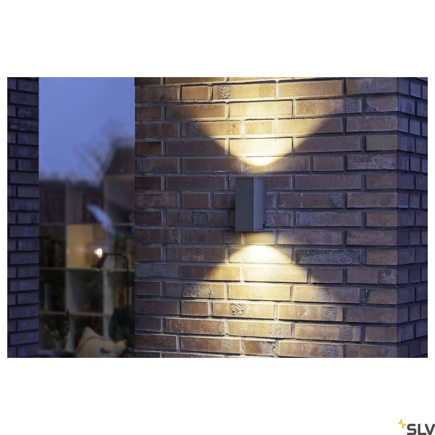 Außenwand mit Backsteinmuster und einer modernen, rechteckigen Außenleuchte, die ein warmes Licht nach oben und unten abstrahlt.