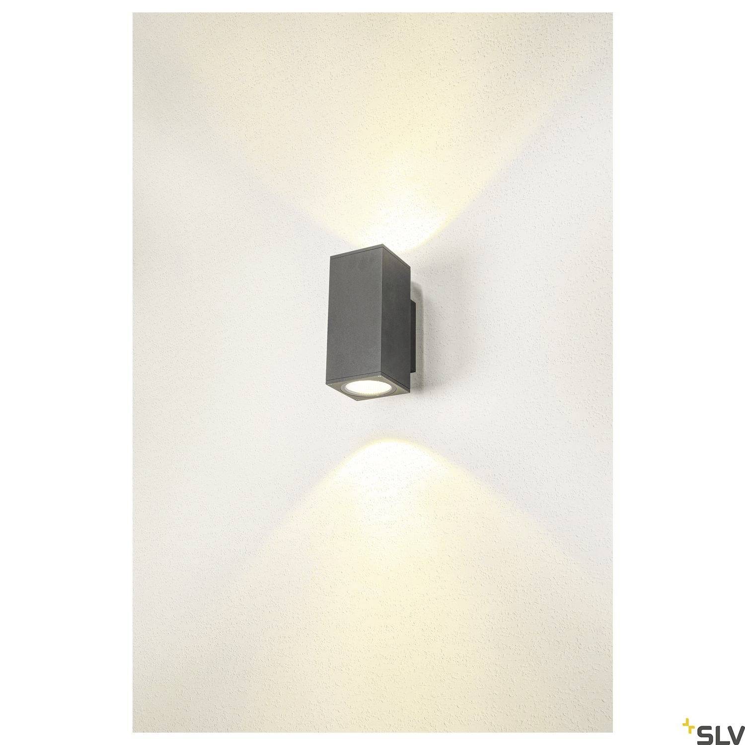 Außenwandleuchte mit rechteckigem Gehäuse in dunklem Grau, wirft Lichtkegel nach oben und unten an weiße Wand.