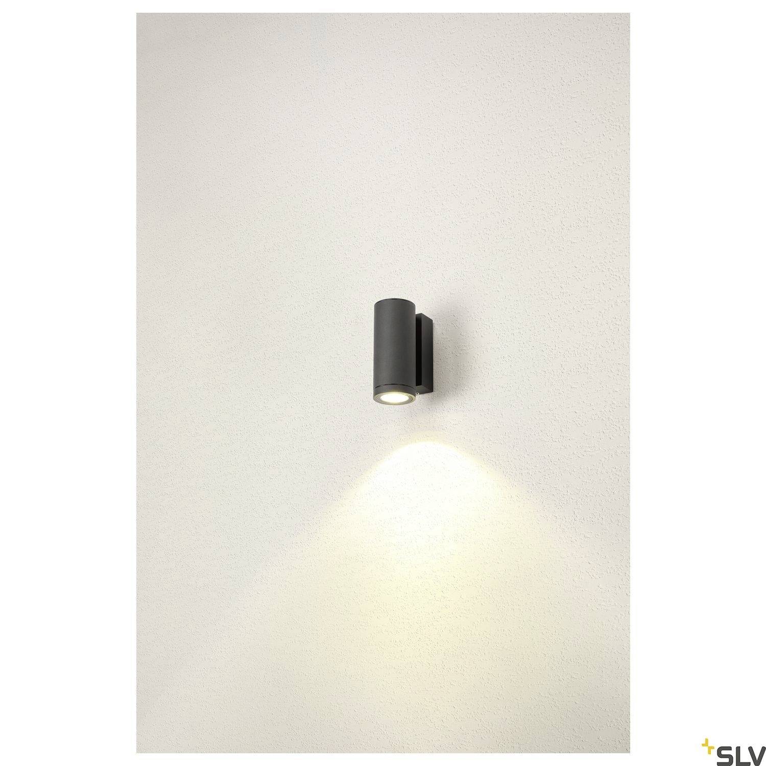 Eine moderne, schwarze Wandleuchte strahlt warmes Licht nach unten auf eine helle Wand.