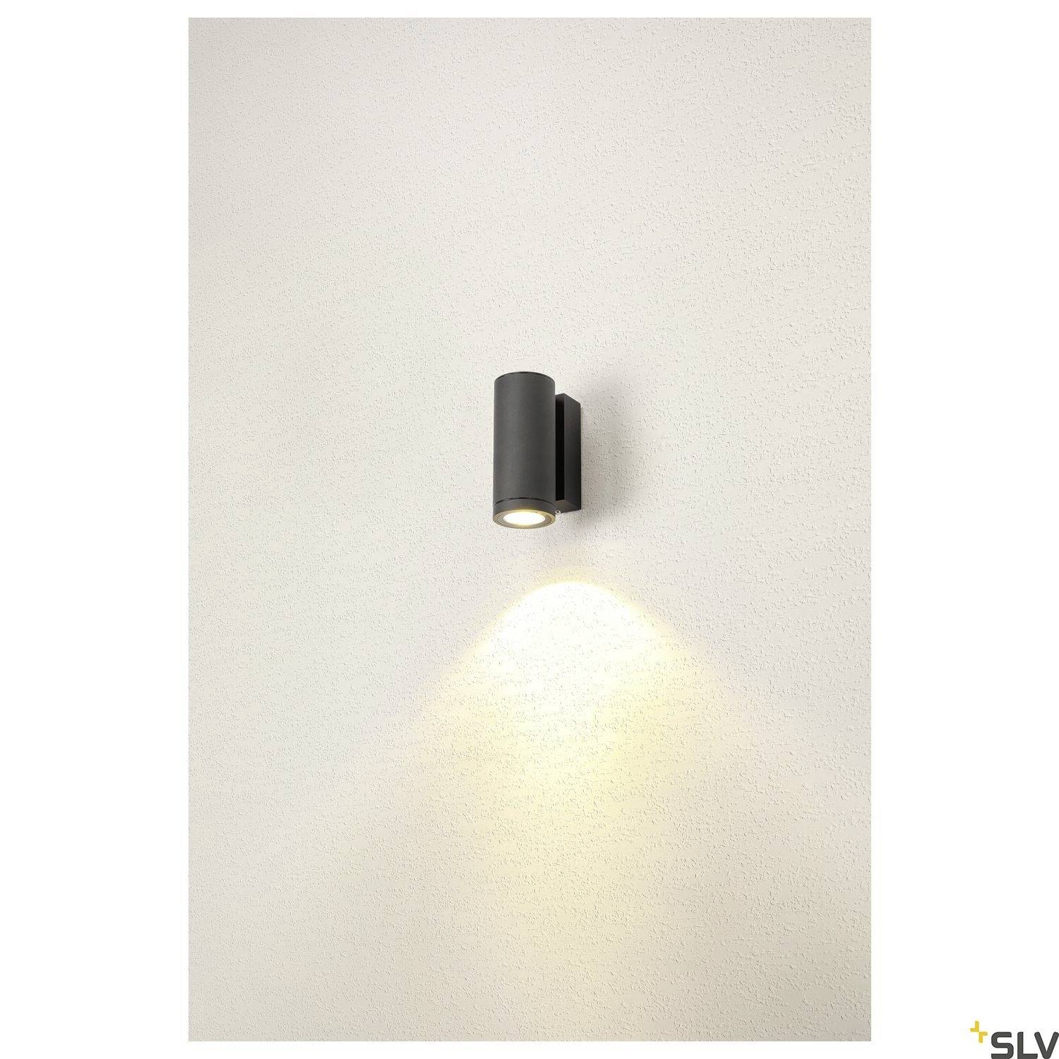 Schwarze, zylinderförmige Wandleuchte auf weißer Wand, strahlt sanft nach unten und oben. Minimalistisches Design für indirekte Beleuchtung.