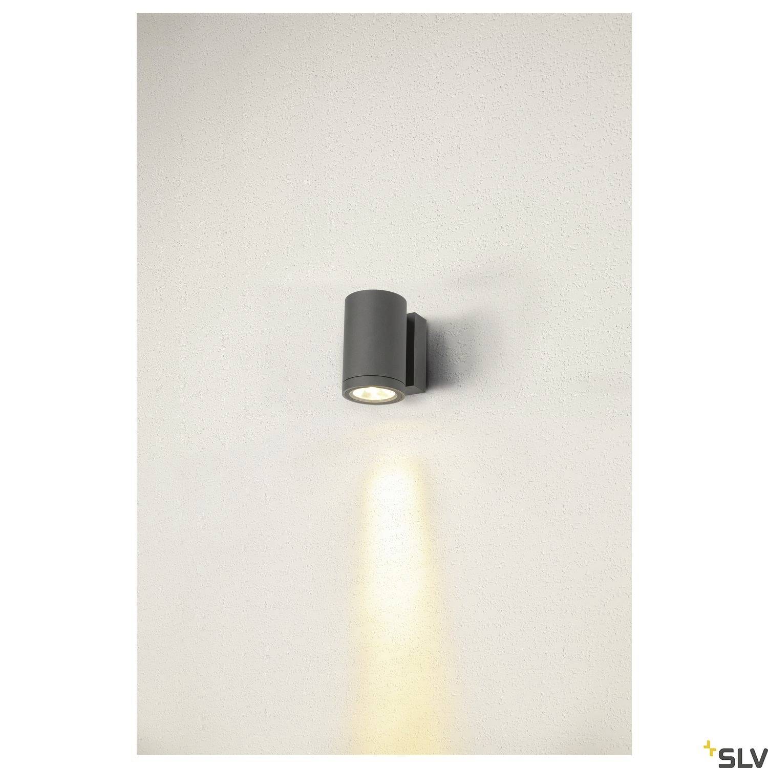 Schwarze zylindrische Wandleuchte an einer beigen Wand, leuchtet nach unten und erzeugt einen Lichtkegel auf der Wandoberfläche.
