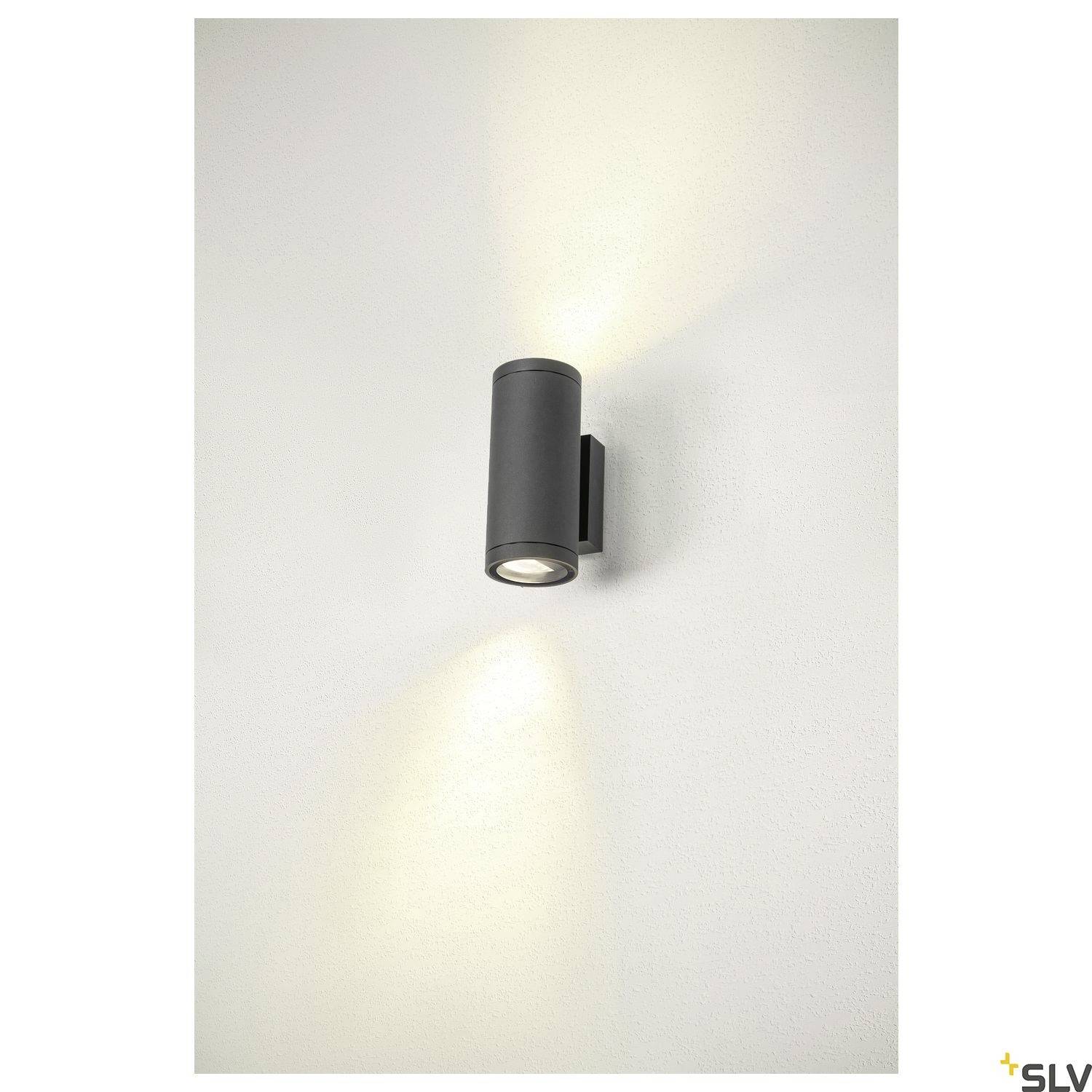 Eine zylindrische schwarze Wandlampe strahlt Licht nach oben und unten gegen eine weiße Wand.