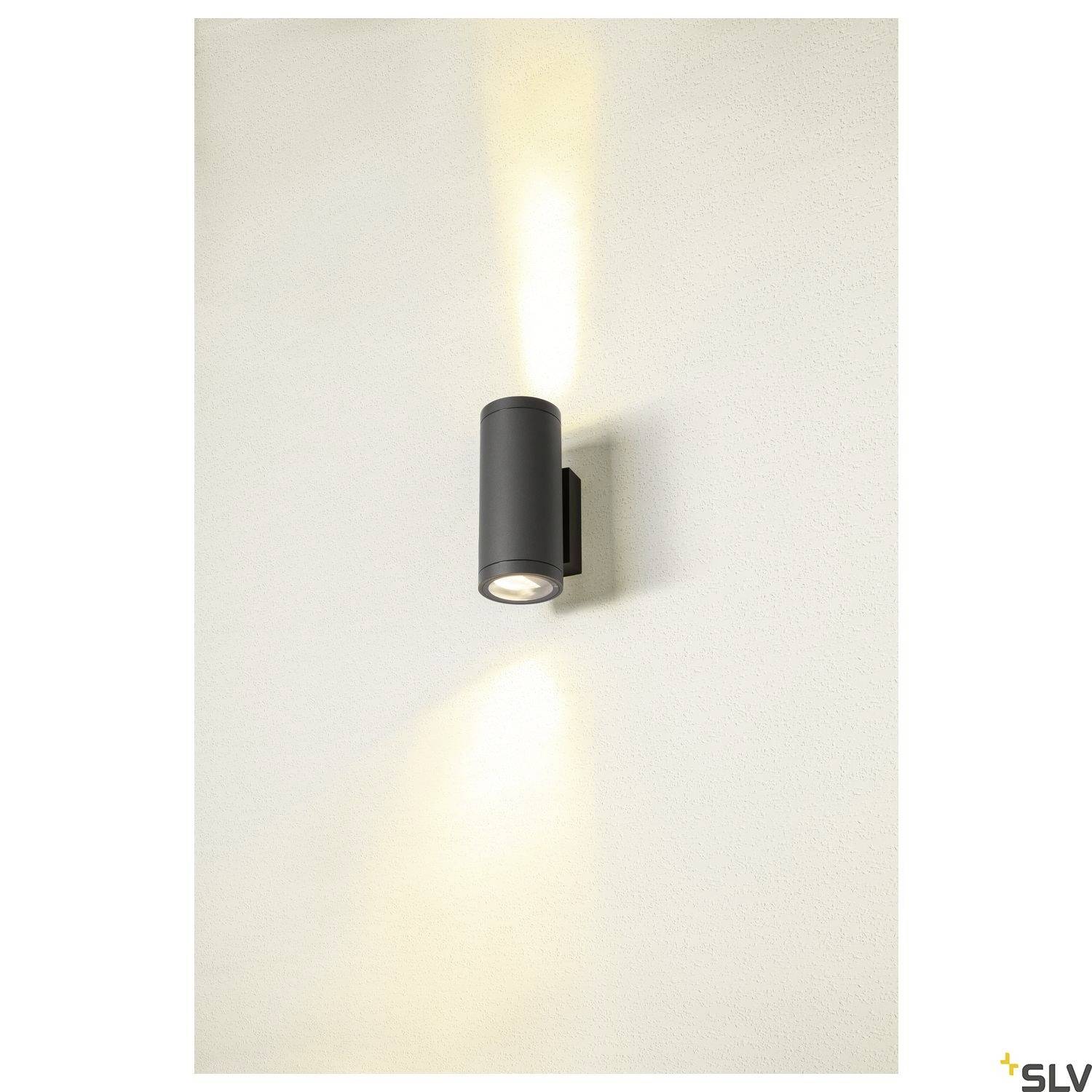 Eine schwarze, zylindrische Wandlampe strahlt Licht nach oben und unten an einer hellen Wand aus.