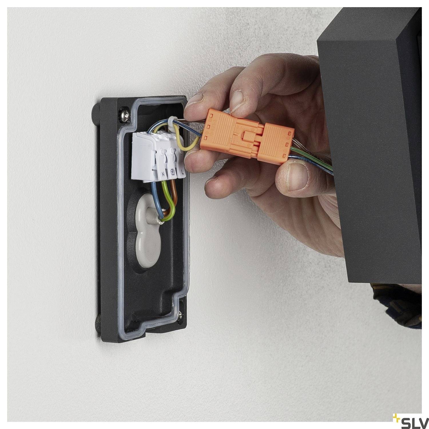Menschliche Hand schließt Wandleuchte an, zeigt Verkabelung; elektrische Installation im Gange, Detailaufnahme der elektrischen Drähte.