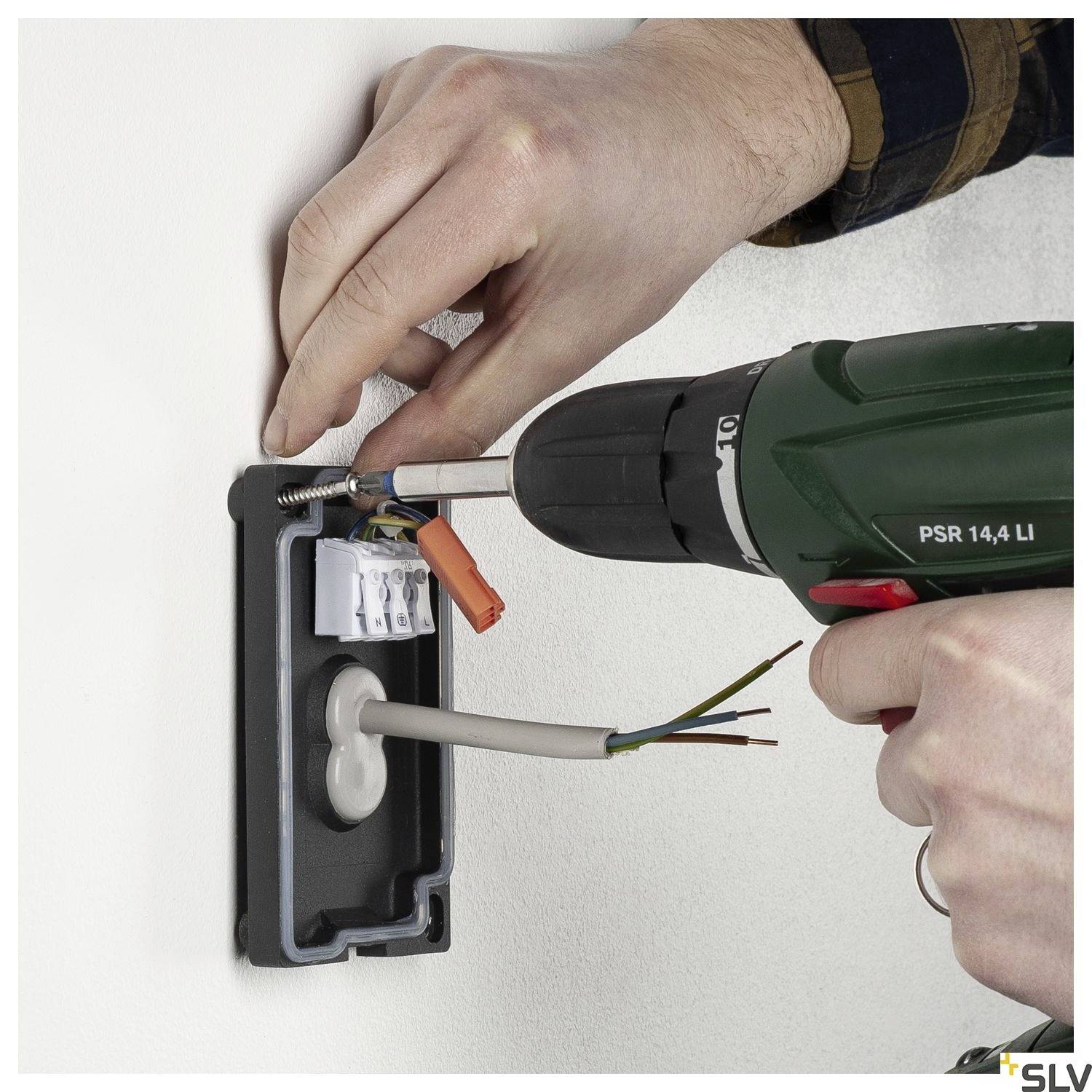 Eine Person installiert eine Steckdose in der Wand mit einem Akkuschrauber. Kabel ragen aus der Wandöffnung heraus.
