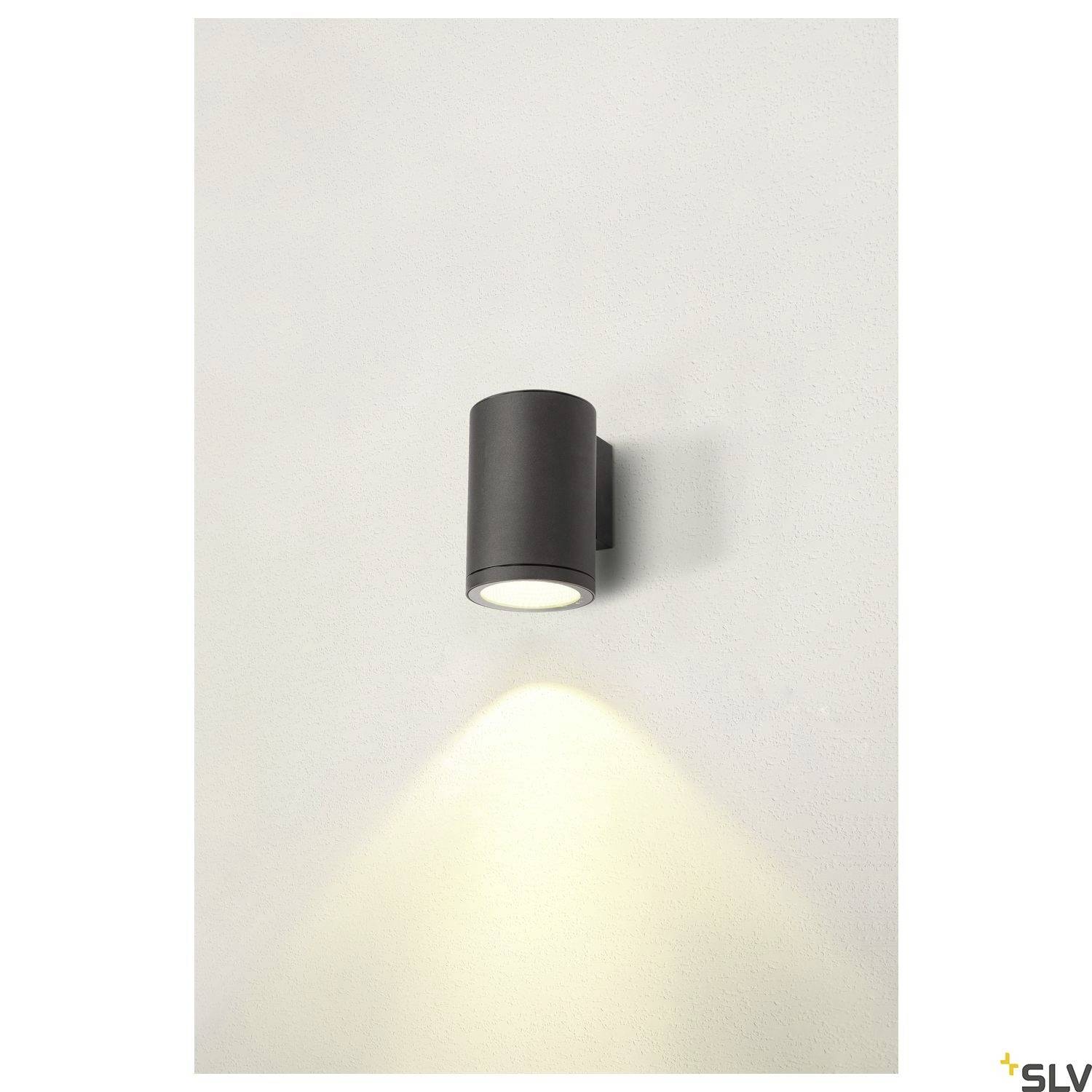 Schwarze Wandlampe leuchtet nach unten und beleuchtet die helle Wand. Minimalistisches Design mit zylindrischer Form.
