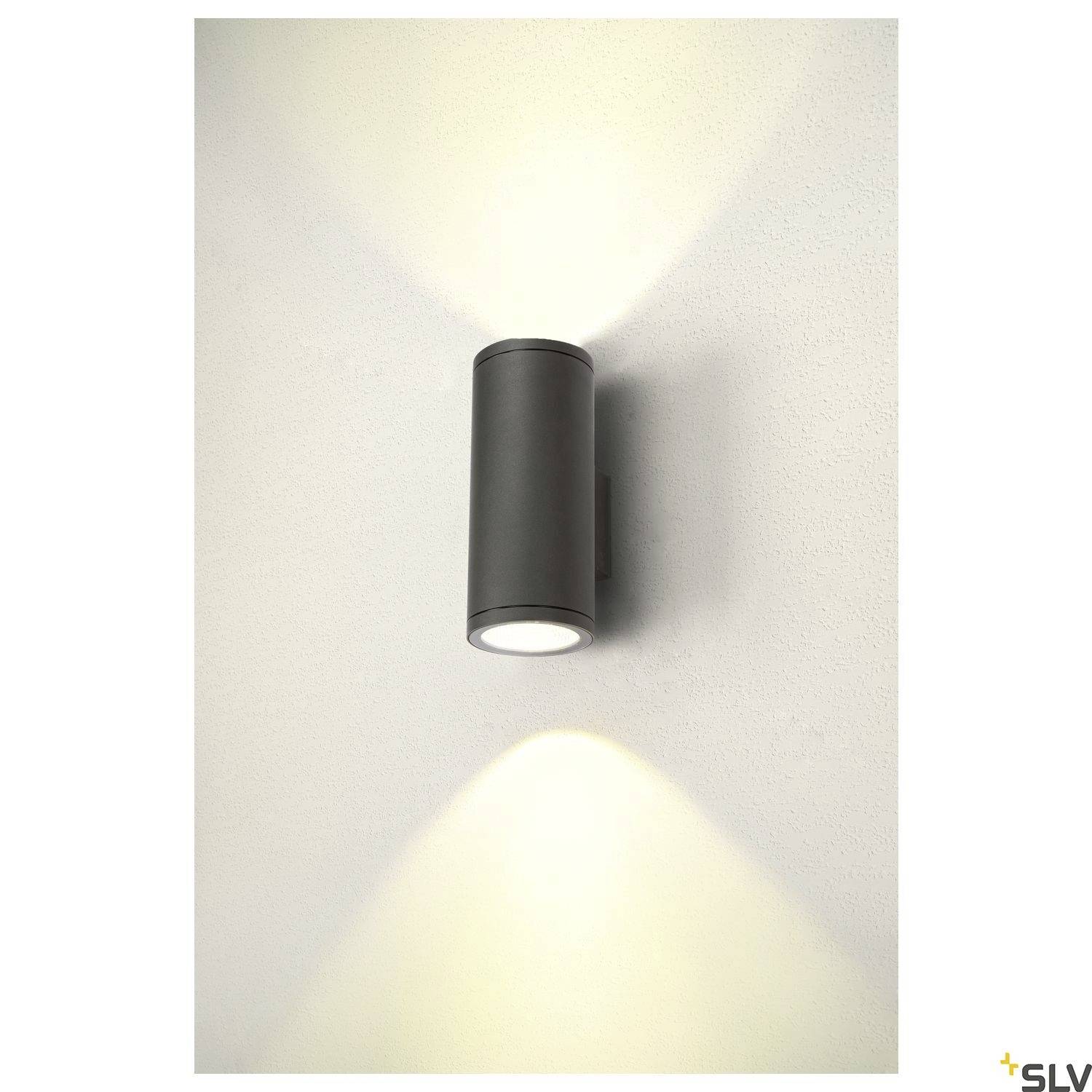 Eine wandmontierte, zylindrische Lampe, die Lichtstrahlen nach oben und unten ausstrahlt, an einer hellen Innenwand montiert.